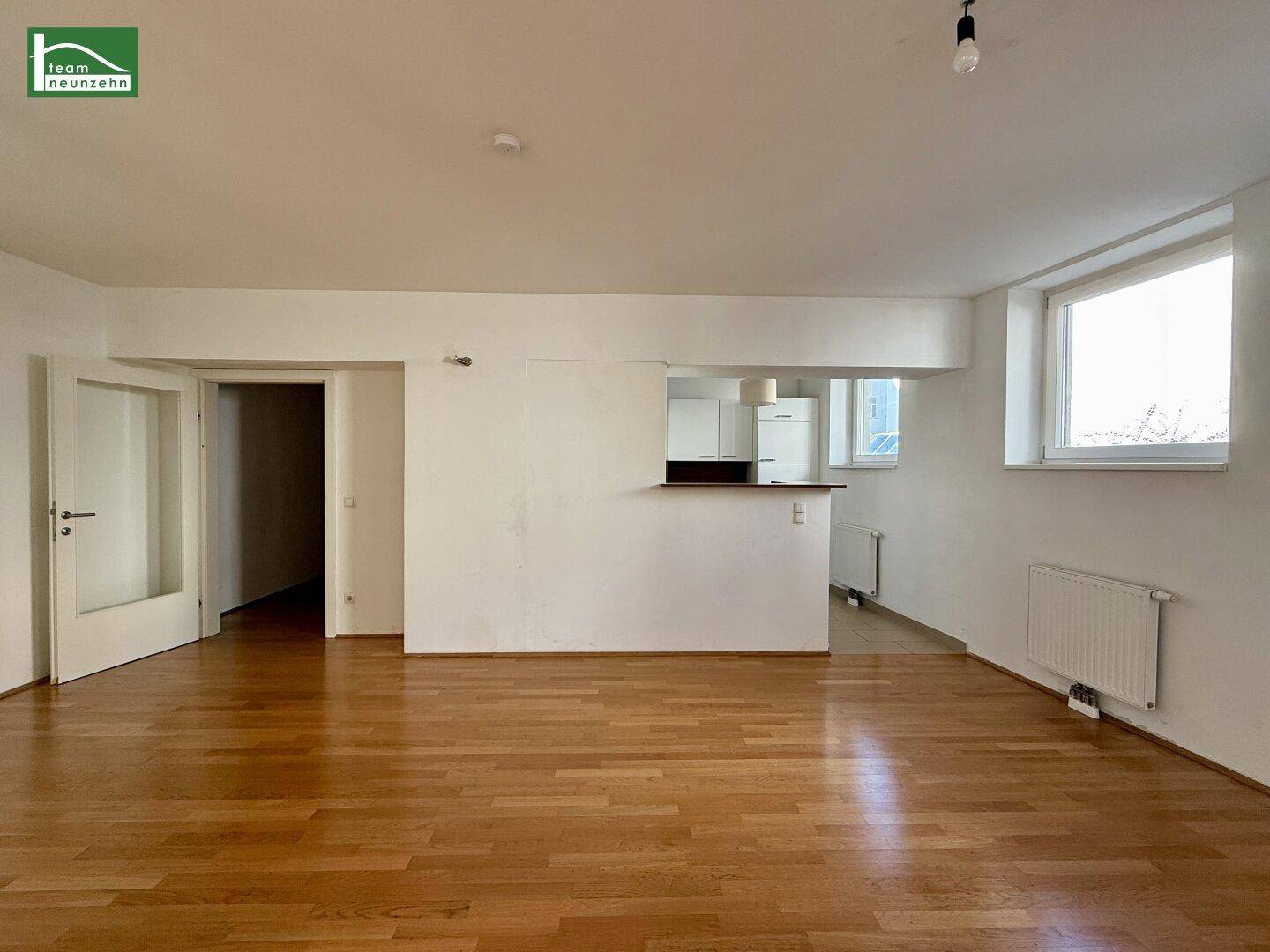 Geräumiger Wohnbereich mit Parkettboden und einer halboffenen Küche mit praktischer Theke.