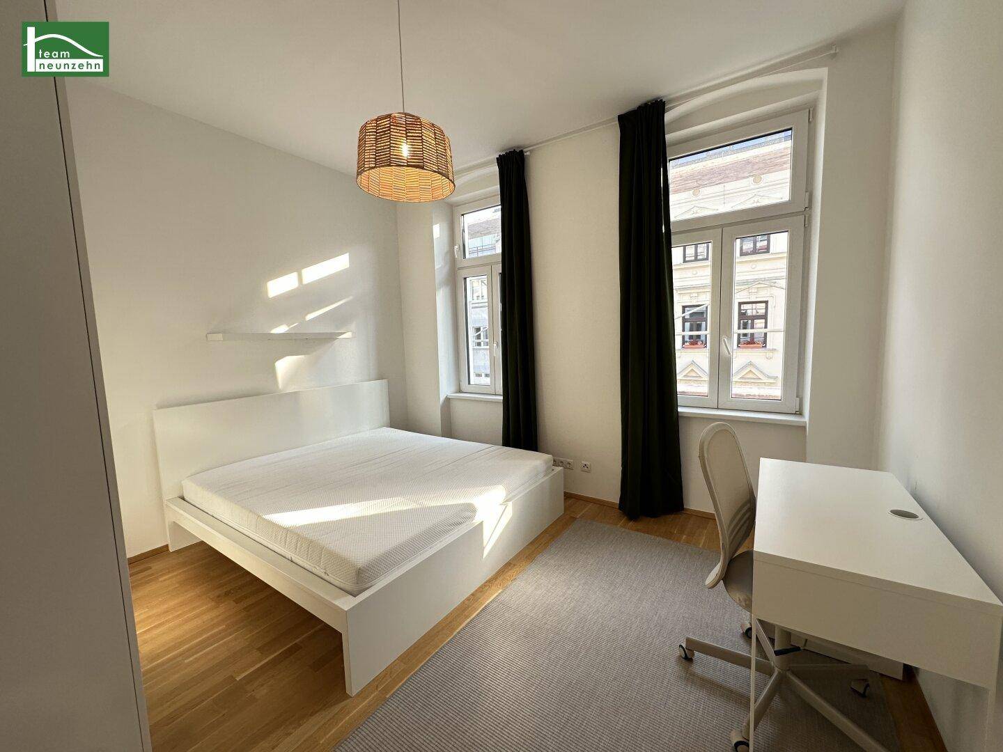 Helles Schlafzimmer mit Doppelbett, Schreibtisch und Blick auf die Stadt.
