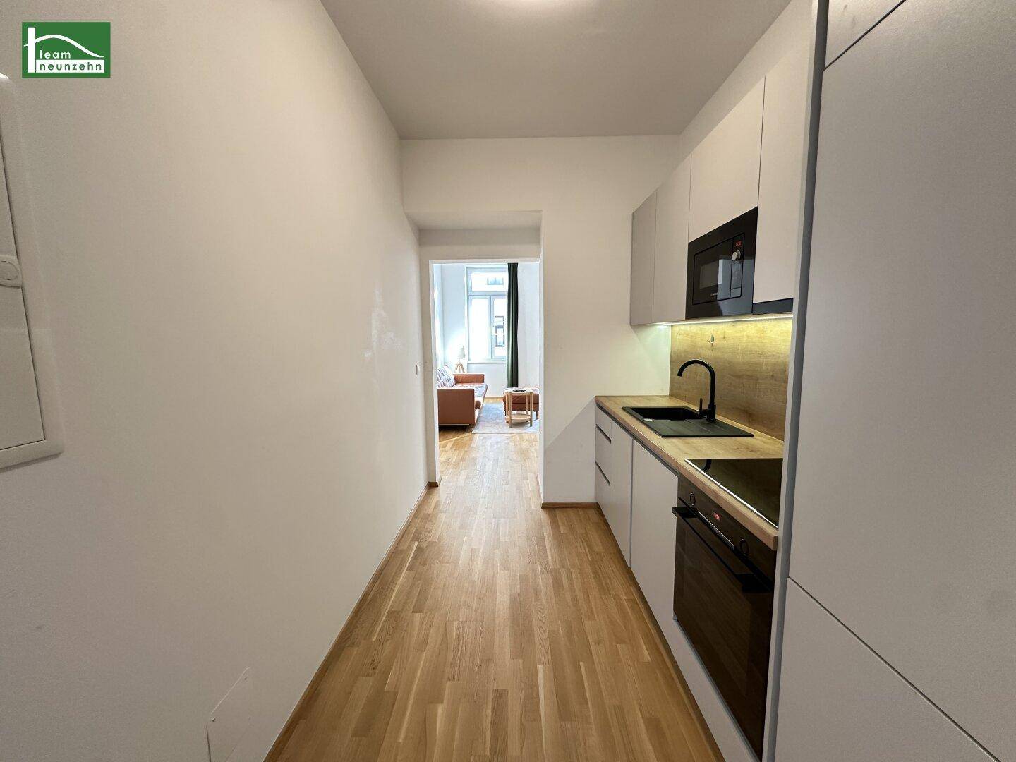 Schmale, moderne Küche mit hellen Schränken, Holzarbeitsplatte und Blick ins Wohnzimmer.