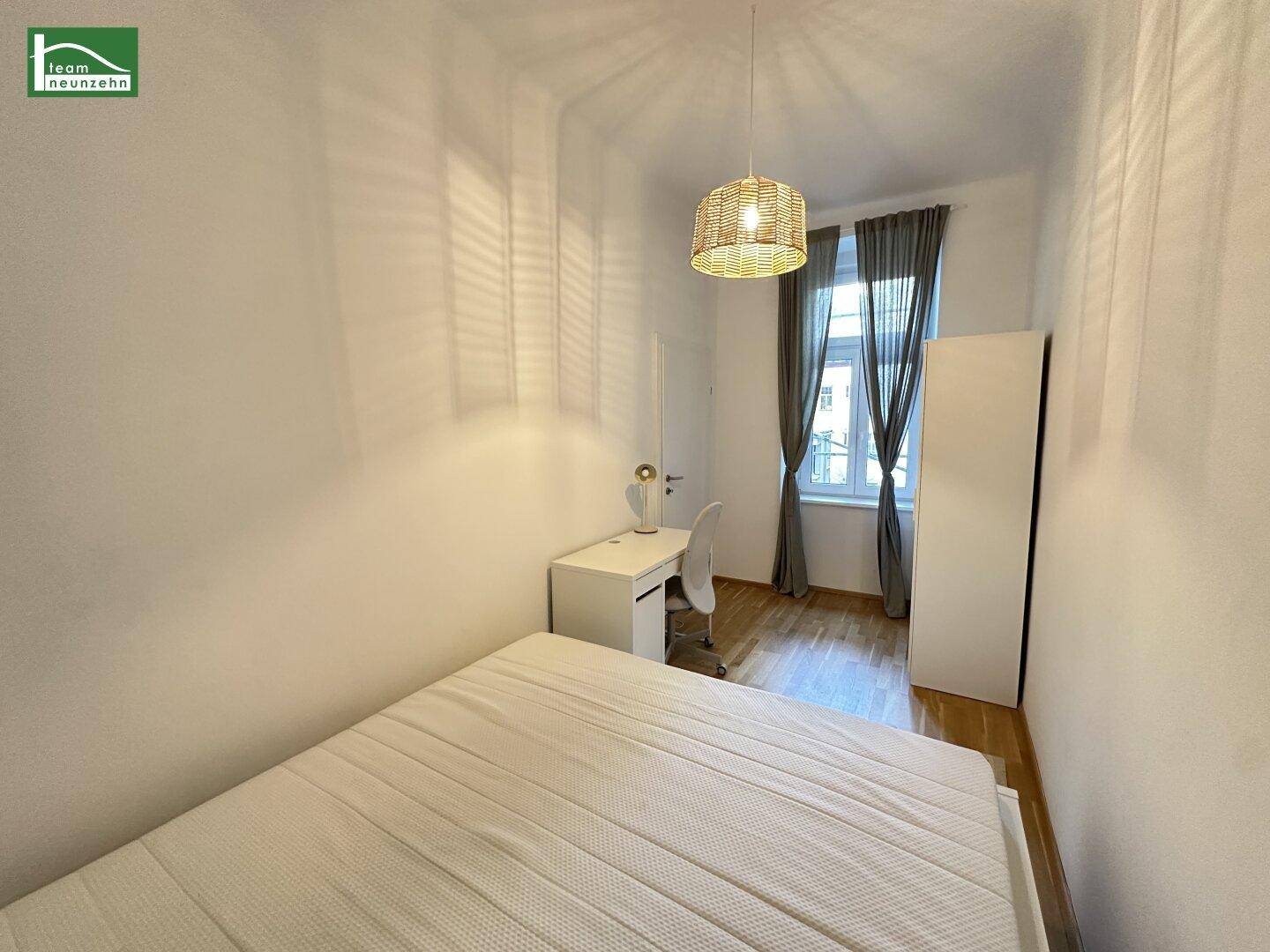 Gemütliches Schlafzimmer mit Holzboden, Schreibtisch und moderner Deckenleuchte.