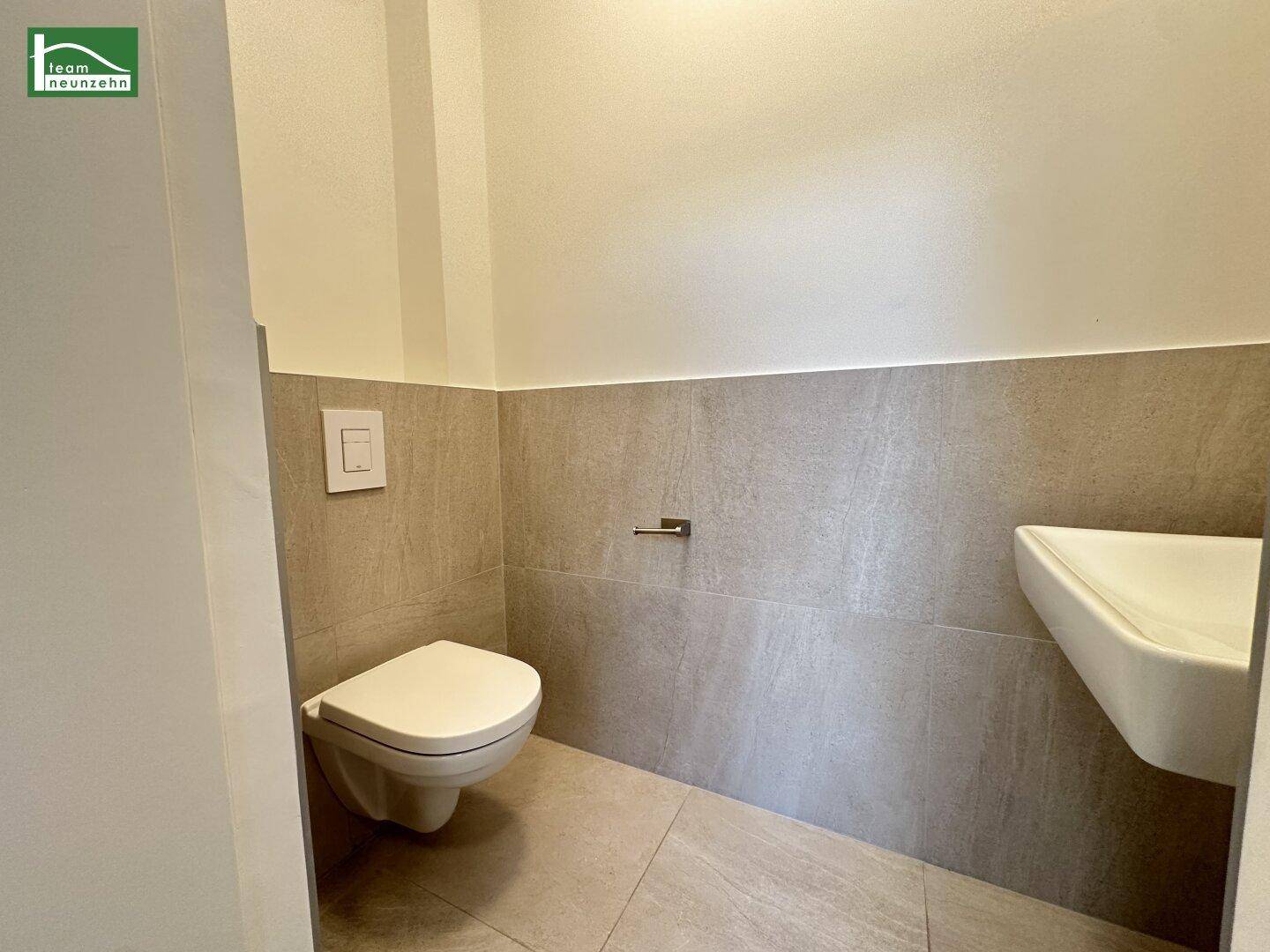 Modernes Gäste-WC mit Wand-WC, kleinem Waschbecken und grauen Fliesen.