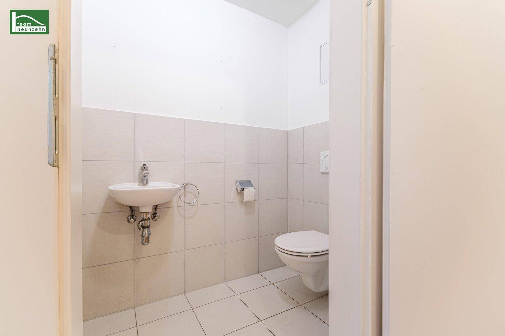 Gäste-WC mit wandhängender Toilette, kleinem Waschbecken und hellen Fliesen.
