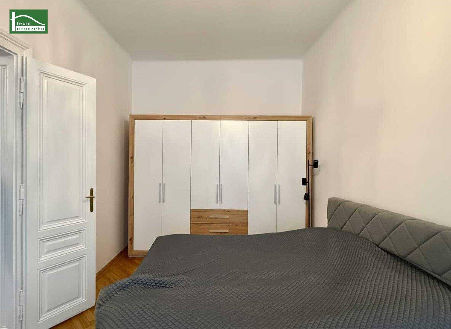 Schlafzimmer mit großem Bett und einem modernen Kleiderschrank mit weißen Türen und Holzrahmen.