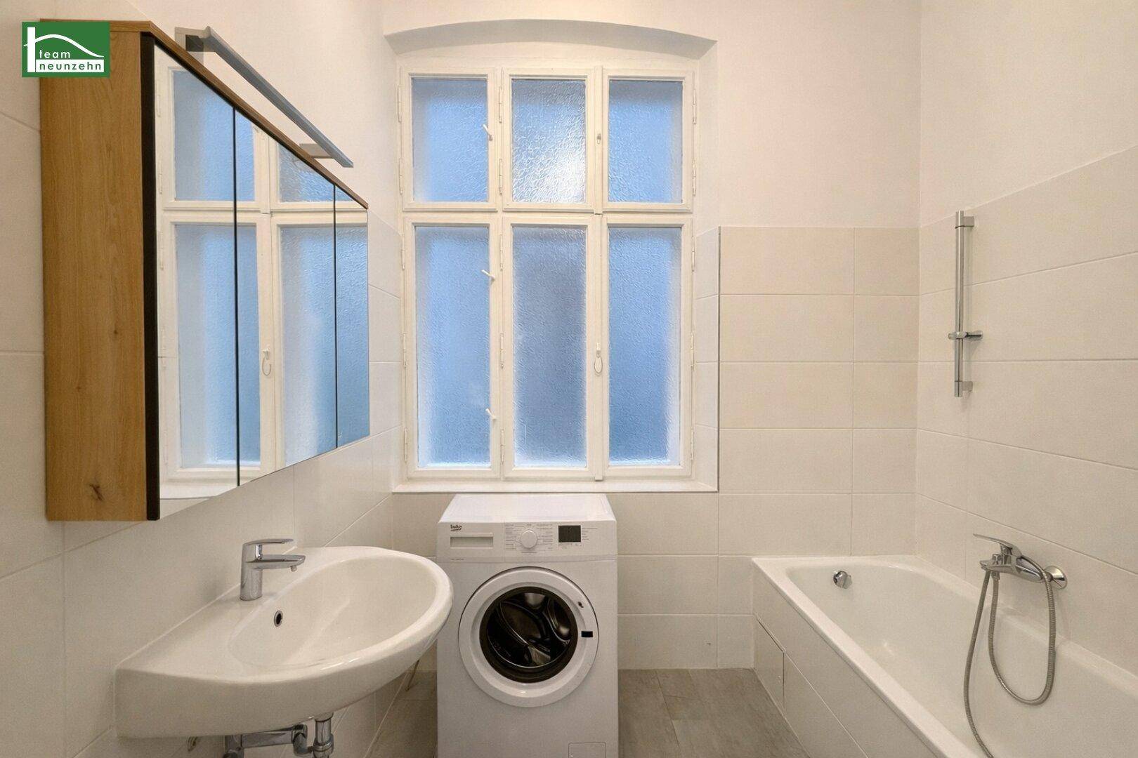 Modernes Badezimmer mit Badewanne, Waschbecken und einer Waschmaschine unter dem Fenster.