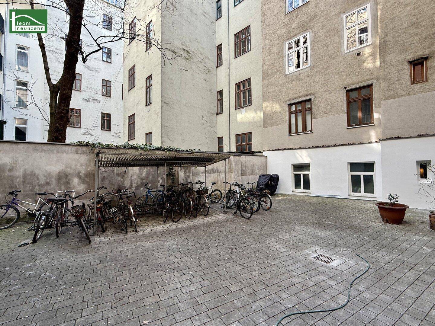 Innenhof mit überdachten Fahrradstellplätzen und der Fassade eines Altbaus bei Sonnenschein.