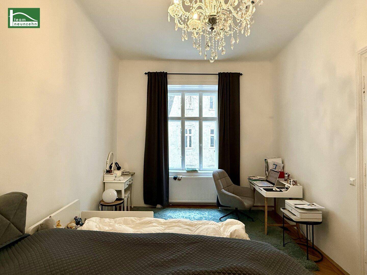 Helles Schlafzimmer mit Schreibtisch, Bett und einem Kronleuchter, der für Eleganz sorgt.