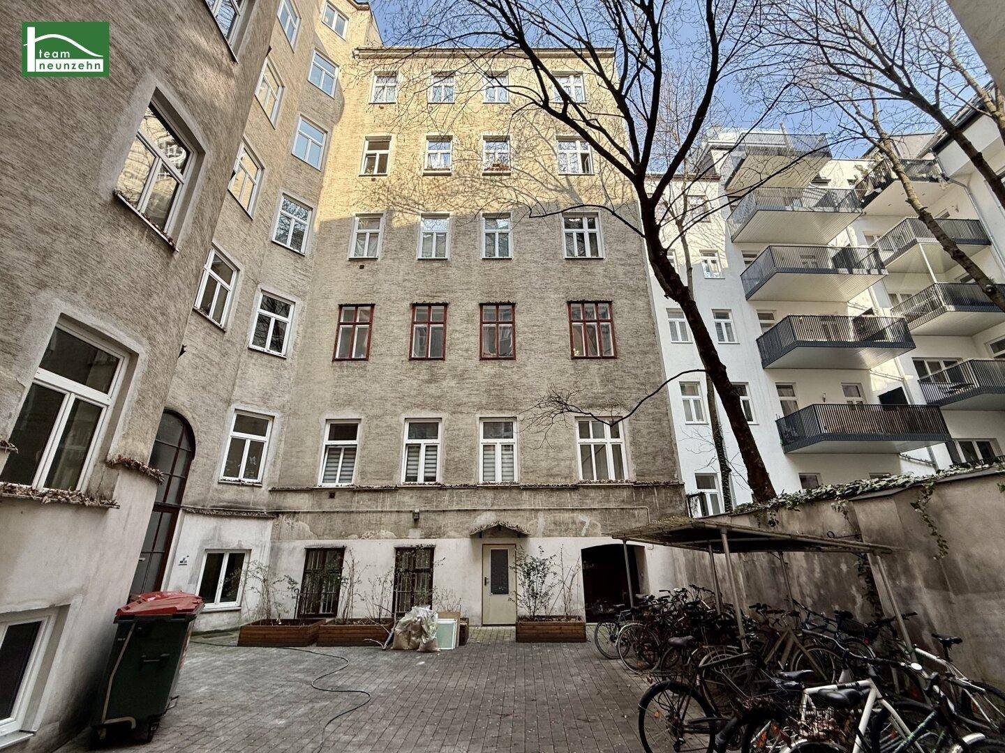 Innenhof eines Mehrfamilienhauses mit Fahrradabstellplätzen und alten Bäumen im Frühling.