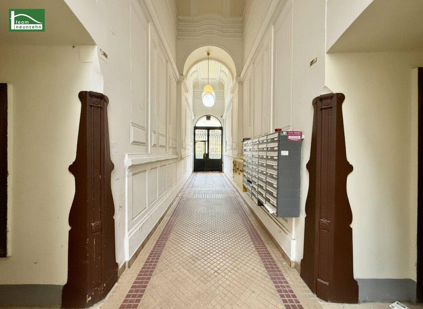Langer, eleganter Eingangsbereich mit historischen Details, Fliesenboden und Briefkästen.