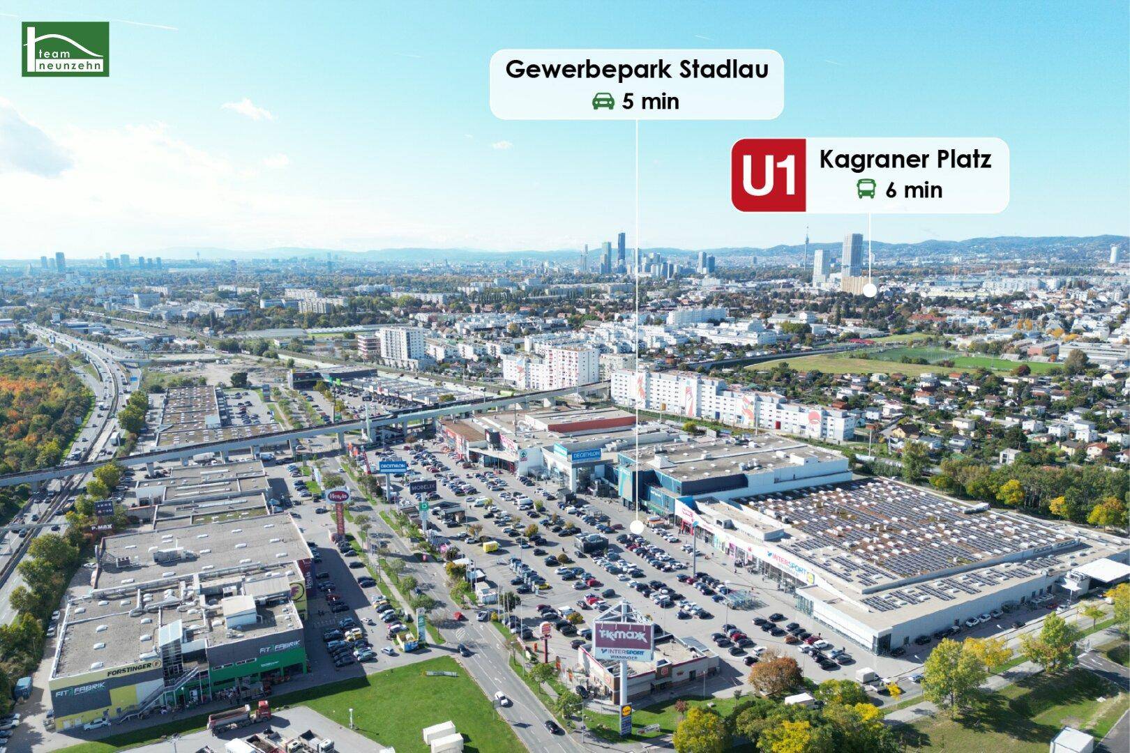 Weitläufiger Gewerbepark mit Einkaufszentren, großen Parkplätzen und der Wiener Skyline im Hintergrund.