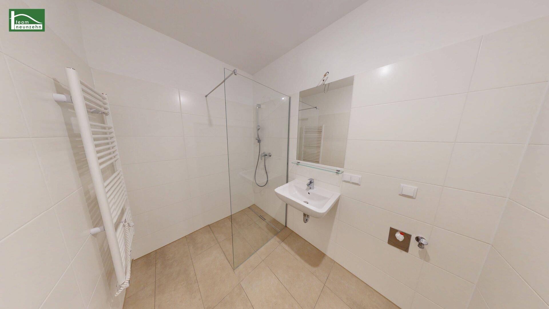 Modernes Badezimmer mit weißen Fliesen, ebenerdiger Dusche und beheiztem Handtuchhalter.