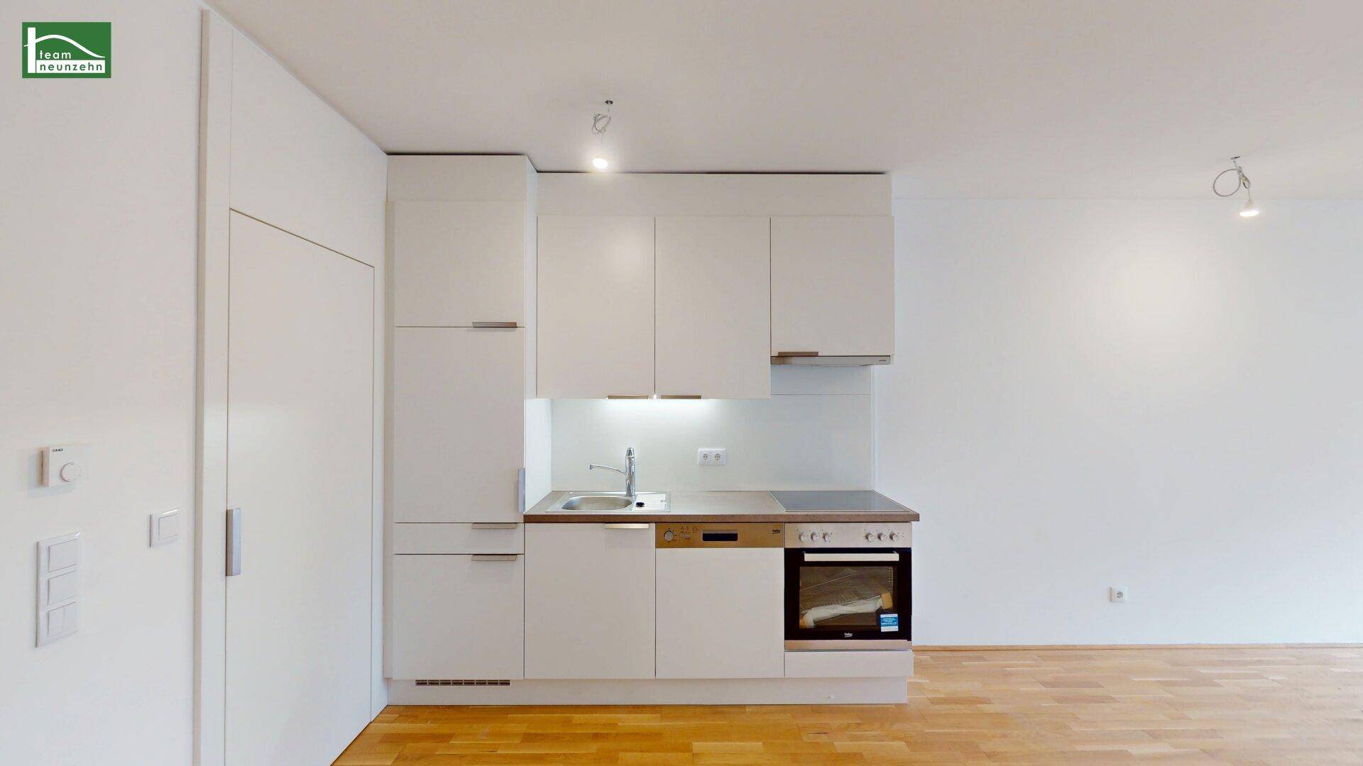 Moderne Küchenzeile mit weißen Schränken, integrierten Geräten und Holzboden.