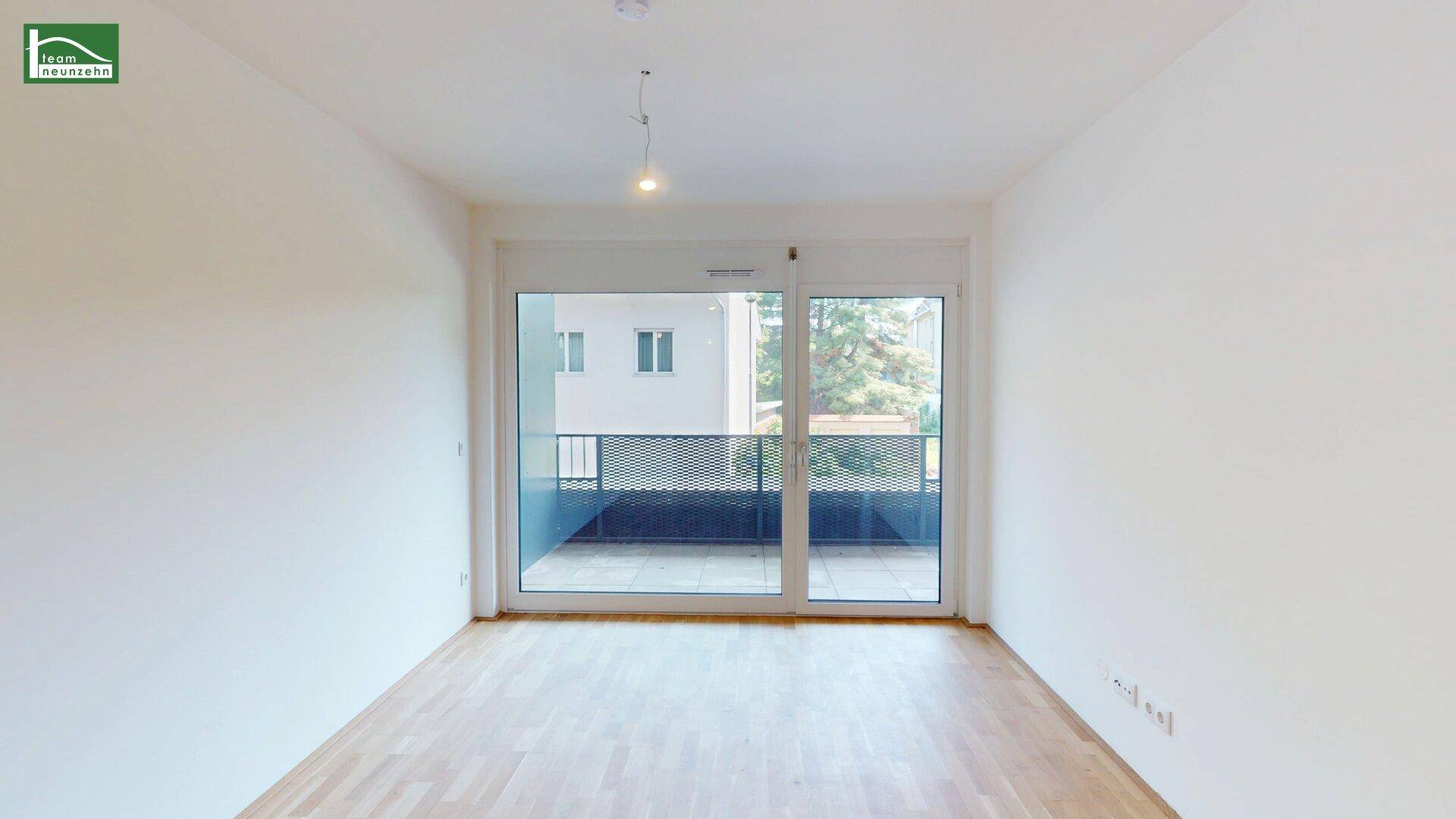 Heller, leerer Raum mit Holzboden und großer Glastür, die zu einem Balkon führt.