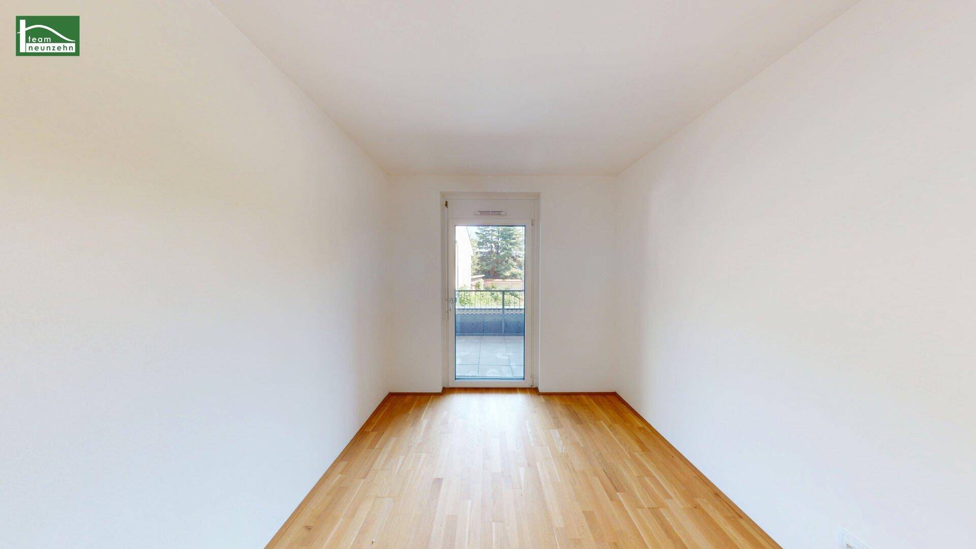 Leerer Raum mit Holzboden und einer Tür, die zu einem kleinen Balkon führt.