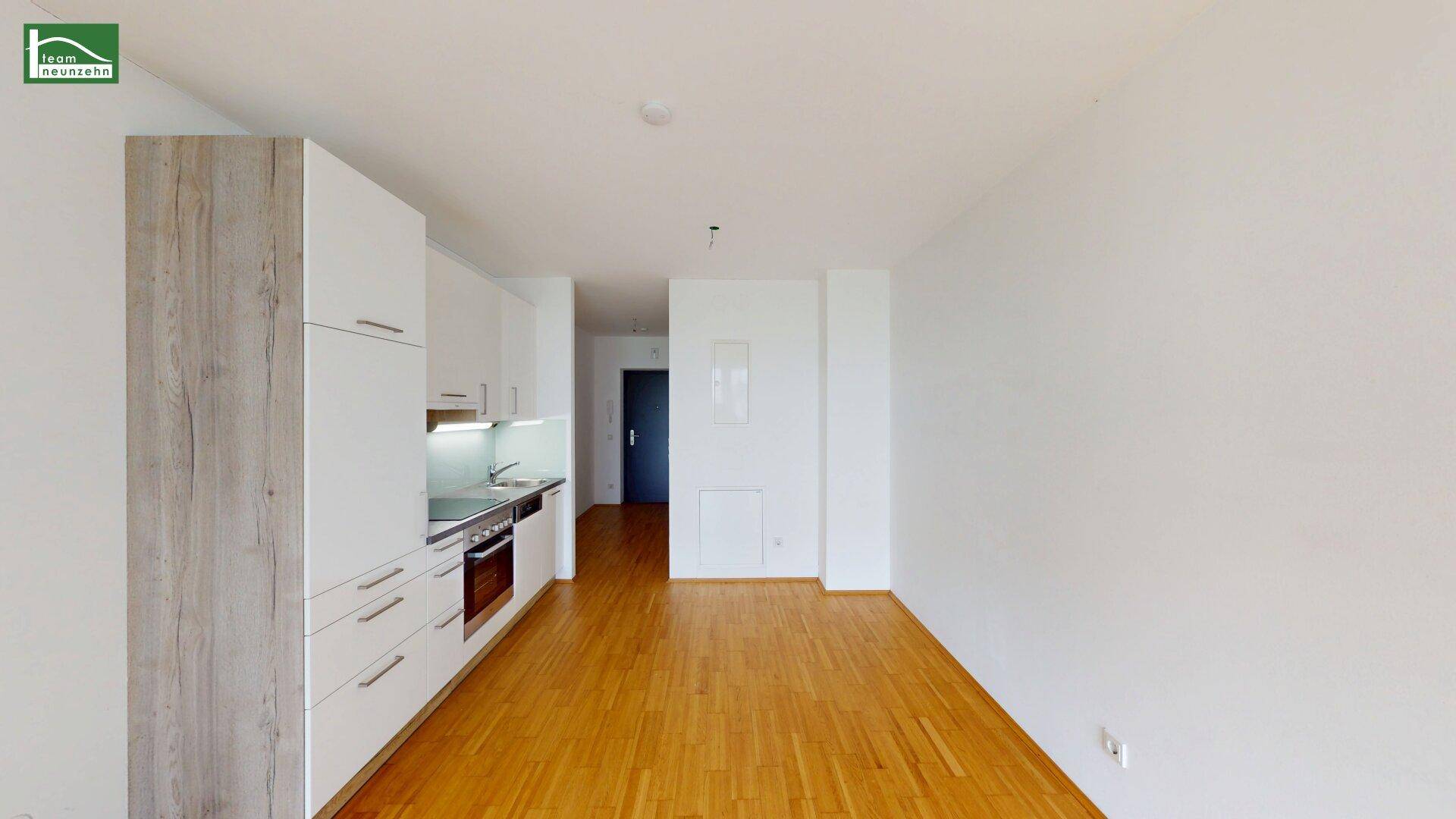 Blick auf die moderne Küchenzeile mit weißen Schränken und den Eingangsbereich mit Holzboden.