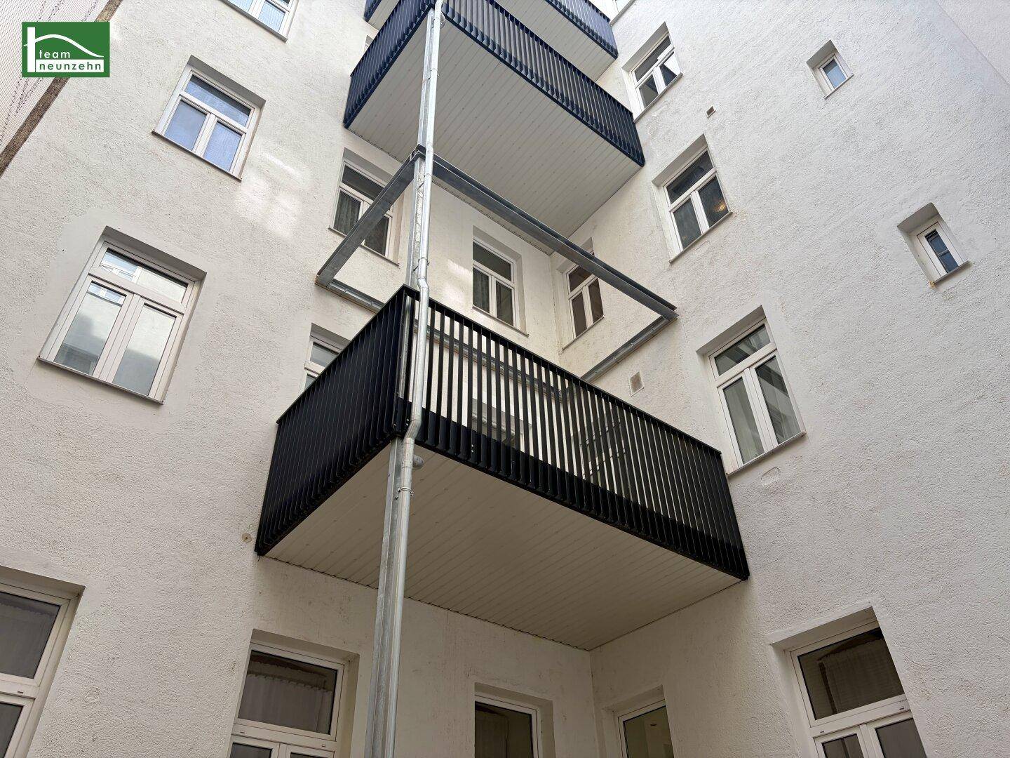 Mehrere moderne Balkone mit schwarzen Geländern an der weißen Fassade eines Mehrfamilienhauses.