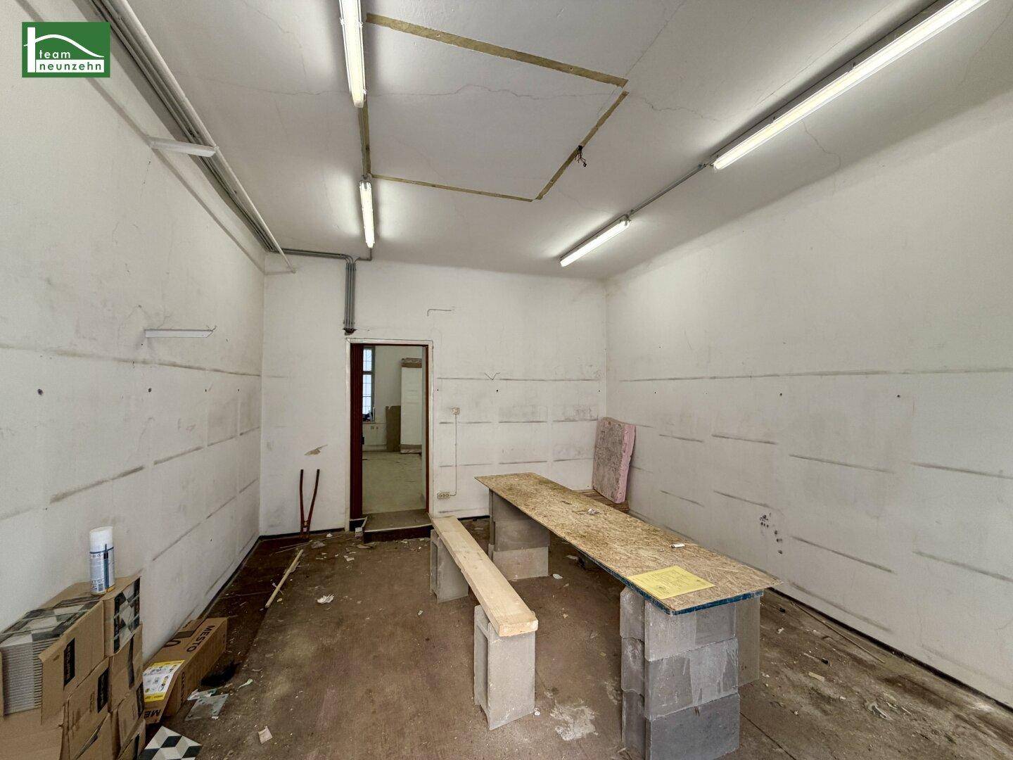Leerer Raum mit einfacher Beleuchtung und provisorischer Arbeitsfläche, in Renovierungsphase.