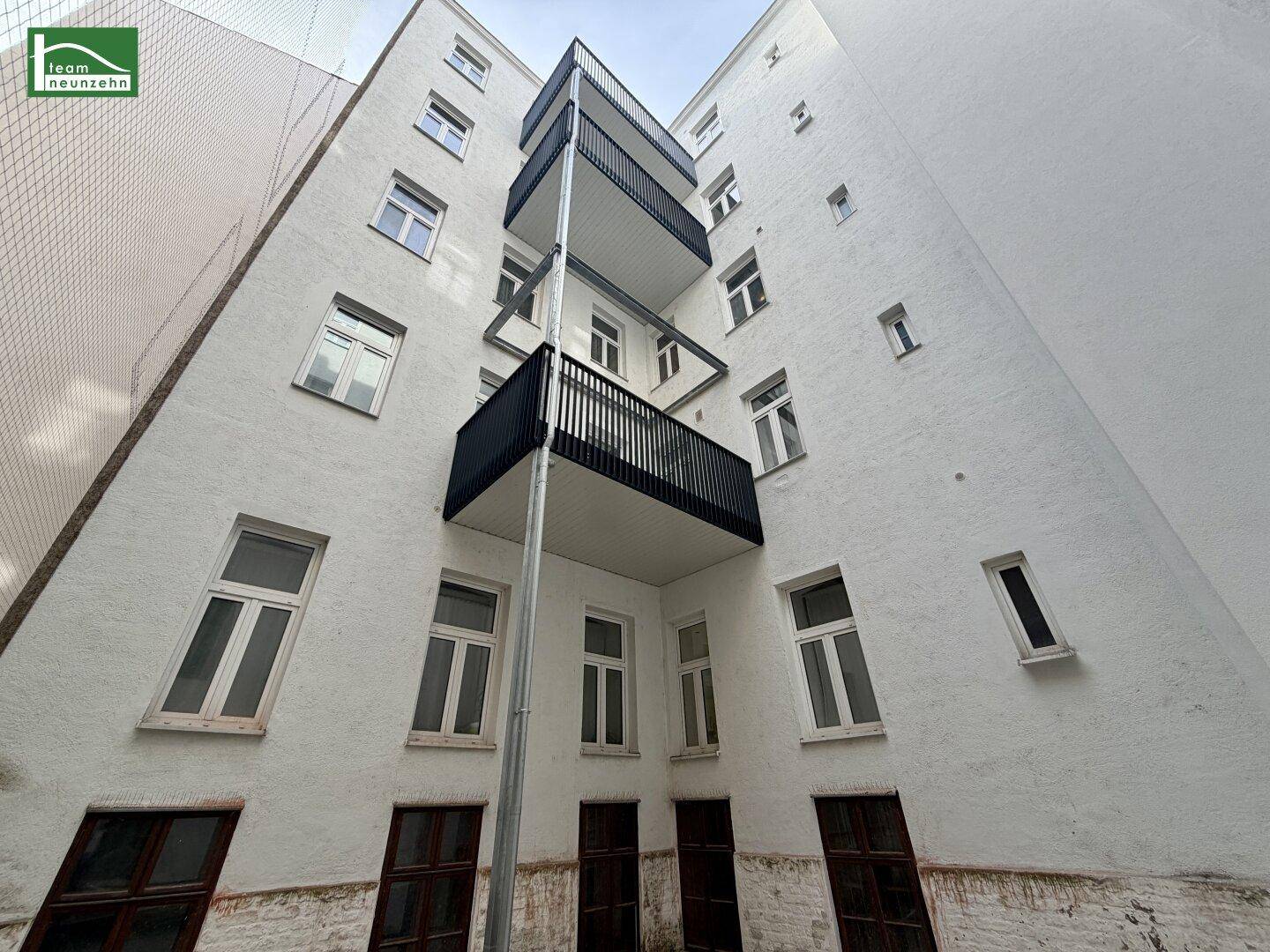 Weiße Gebäudefassade mit mehreren übereinanderliegenden Balkonen und vielen Fenstern.