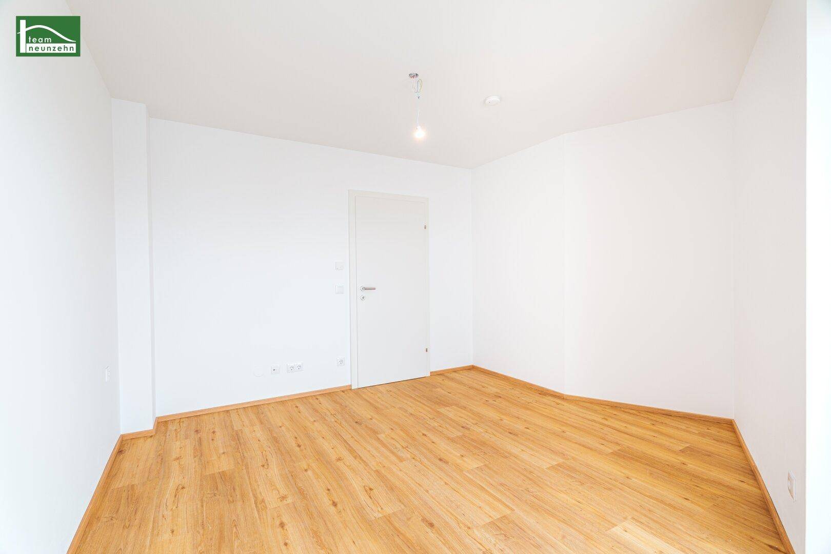 Leeres Zimmer mit Holzboden und weißer Tür, bereit zur individuellen Gestaltung.