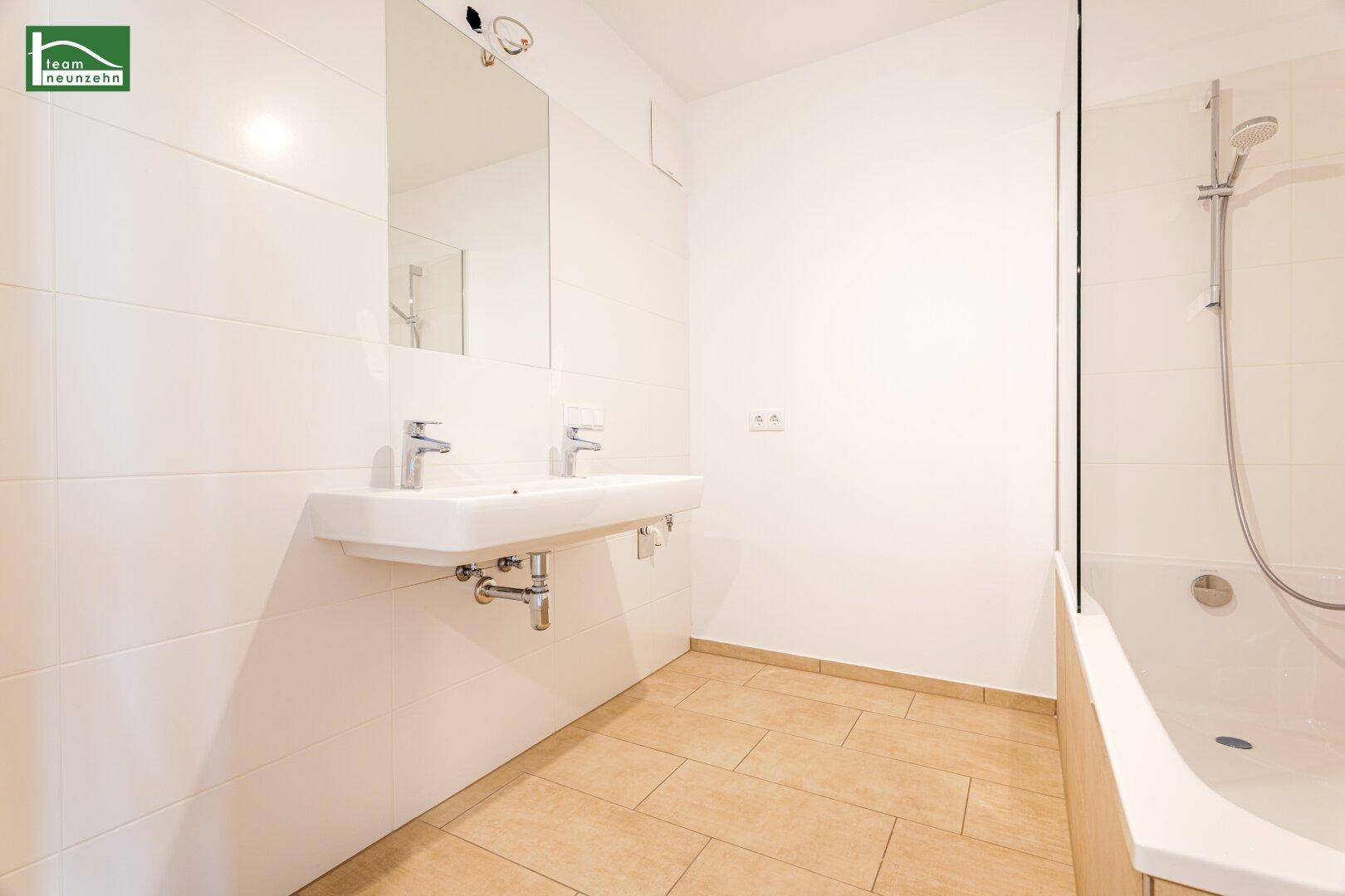 Modernes Badezimmer mit Doppelwaschbecken, Badewanne und hellen Fliesen.