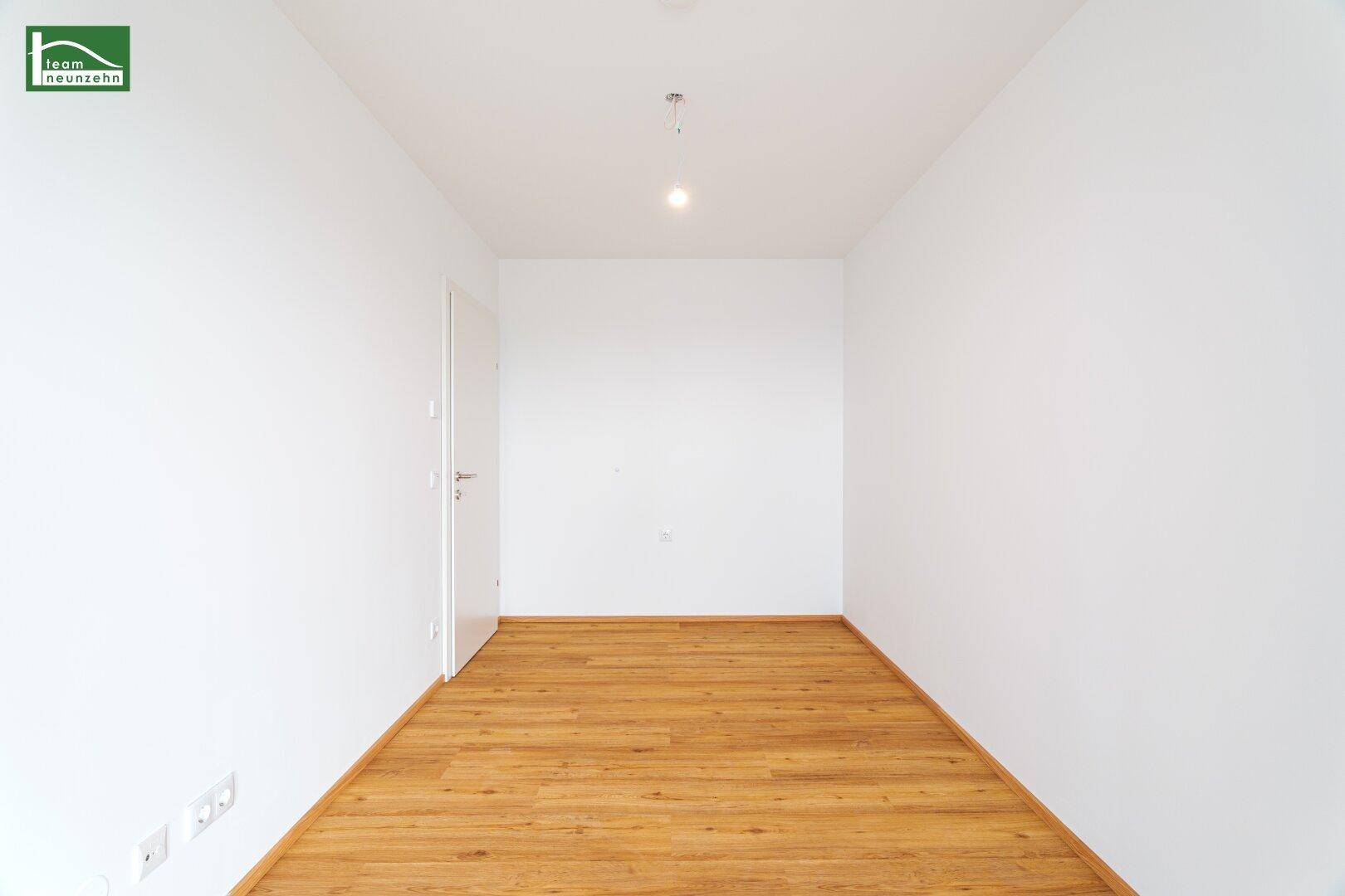 Unmöbliertes Zimmer mit hellem Holzfußboden und weiß gestrichenen Wänden.