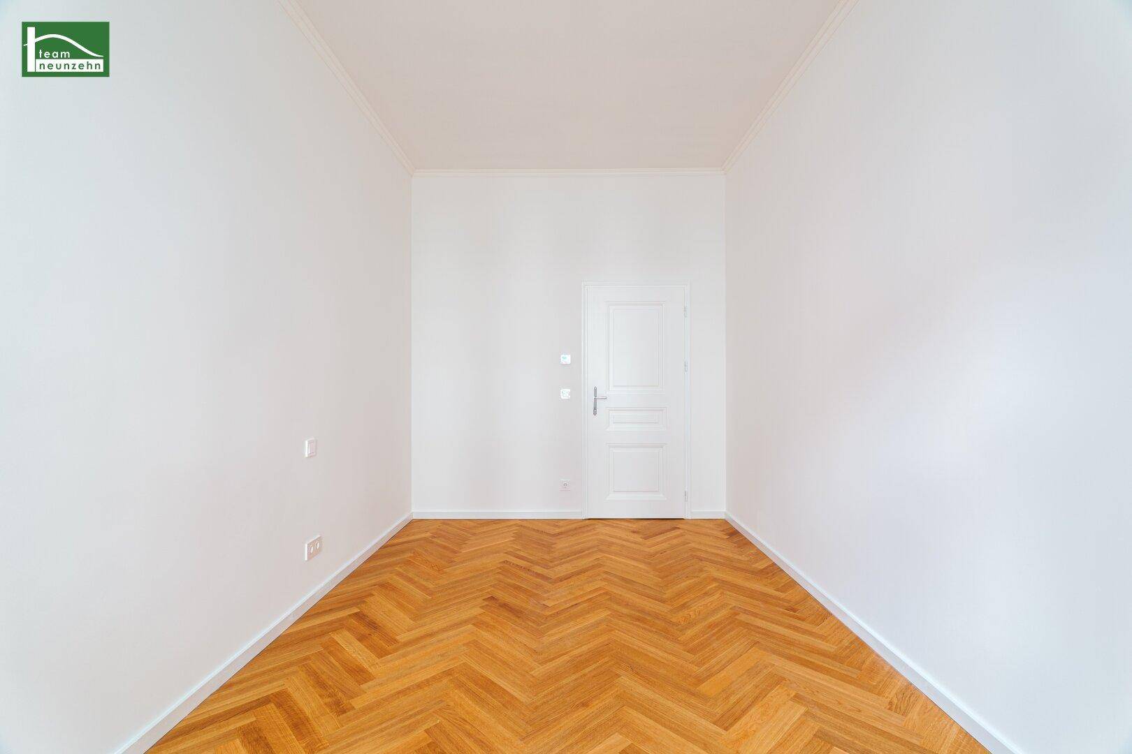 Leeres Zimmer mit Fischgrätparkett und einer Tür, bereit zur individuellen Gestaltung.