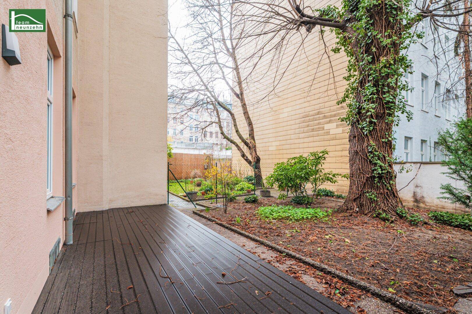 Außenbereich mit Holzterrasse und angrenzendem Garten mit Bäumen und Sträuchern.