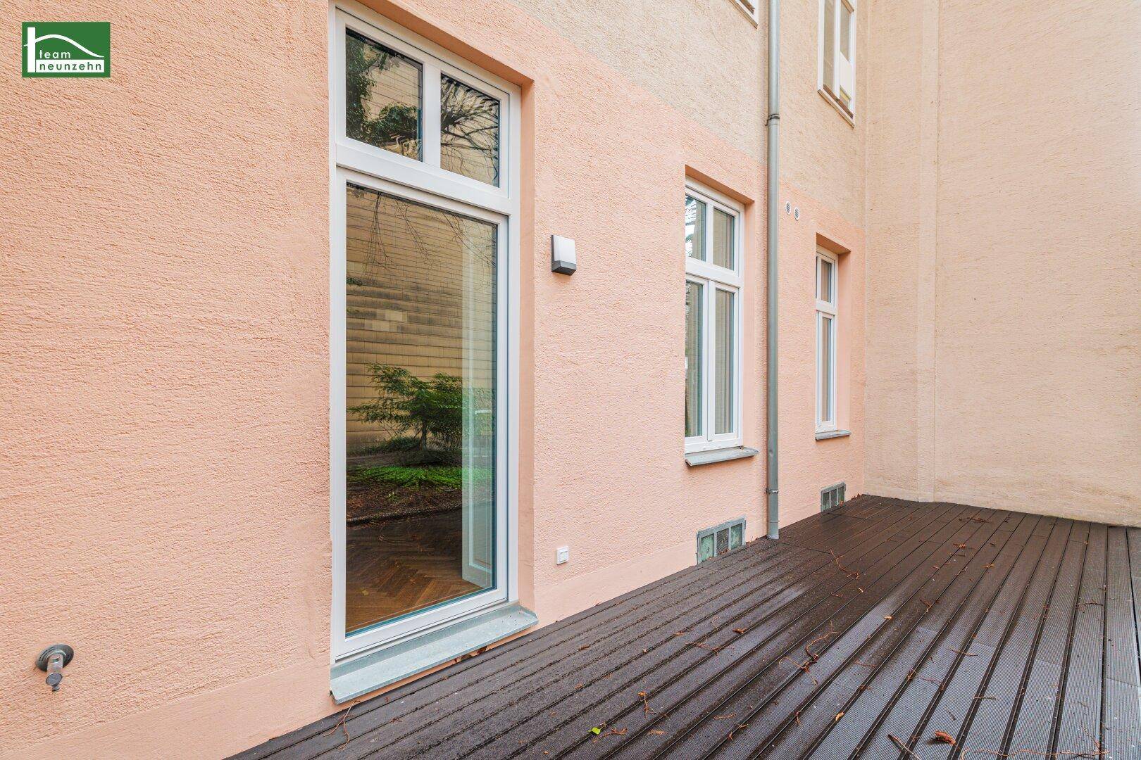 Geräumige Holzterrasse am Gebäude mit Zugang zu einem kleinen Gartenbereich.