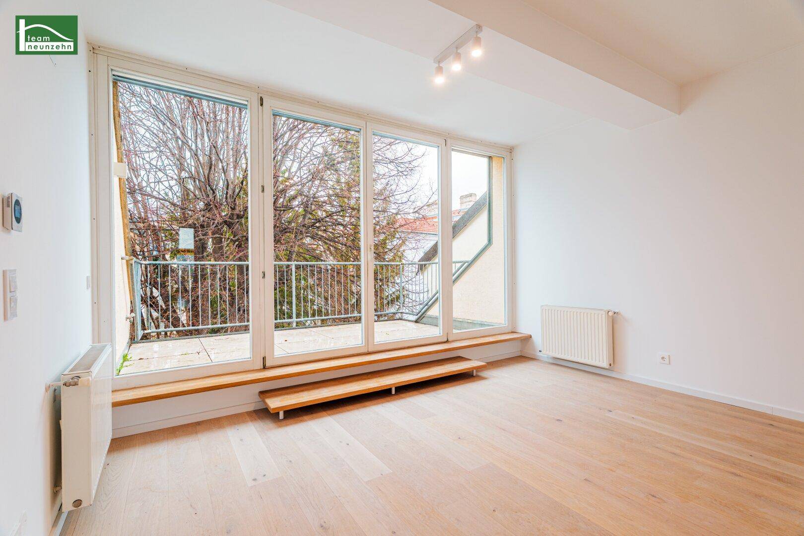 Heller Wohnbereich mit großen Fenstern und direktem Zugang zum Balkon, ideal für natürliches Licht.