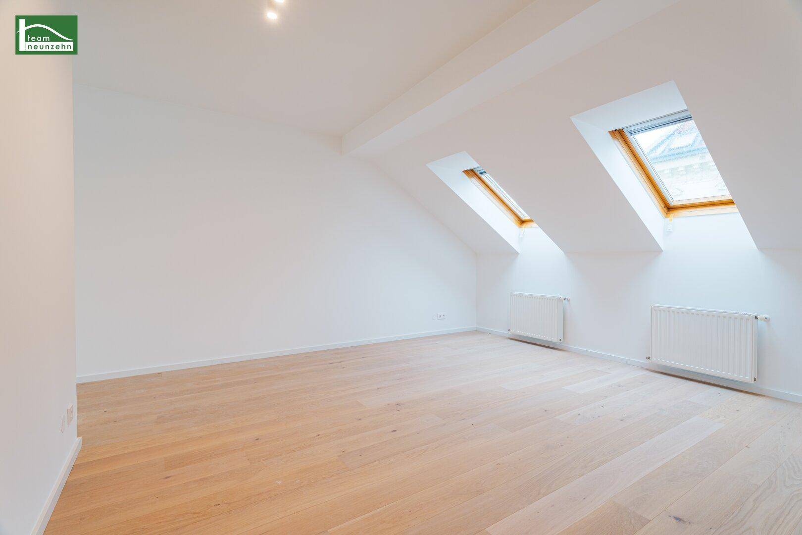 Ruhiges Zimmer im Dachgeschoss mit zwei Dachfenstern und hellem Holzfußboden.
