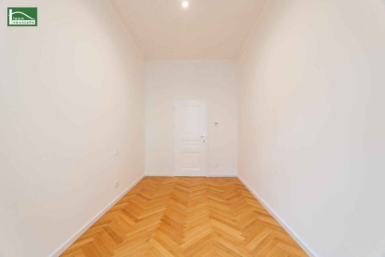 Renoviertes Zimmer mit Fischgrätparkett und weißer Tür, bietet vielseitige Nutzungsmöglichkeiten.
