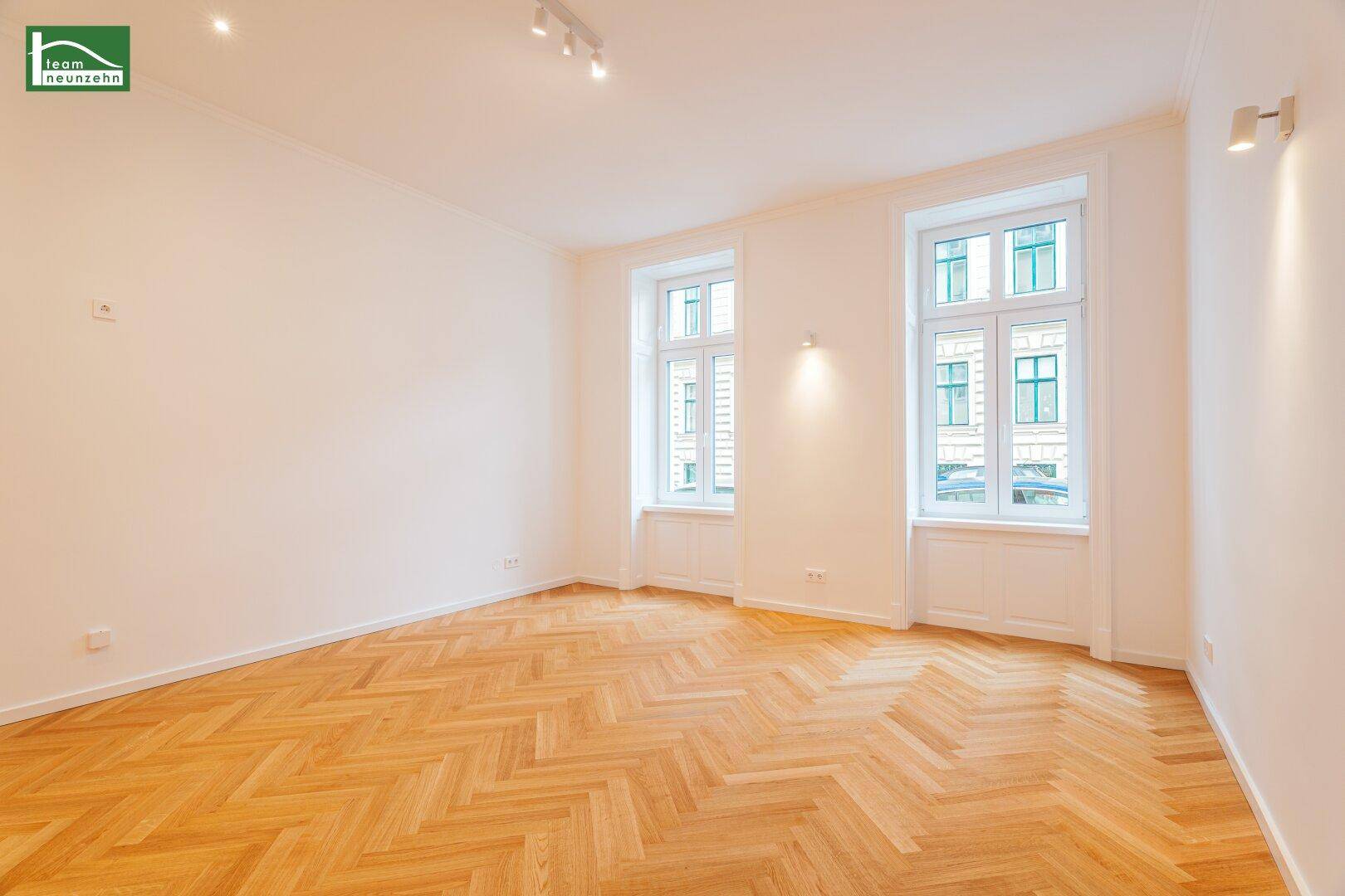 Geräumiges, helles Zimmer mit Fischgrätparkett und moderner Deckenbeleuchtung.
