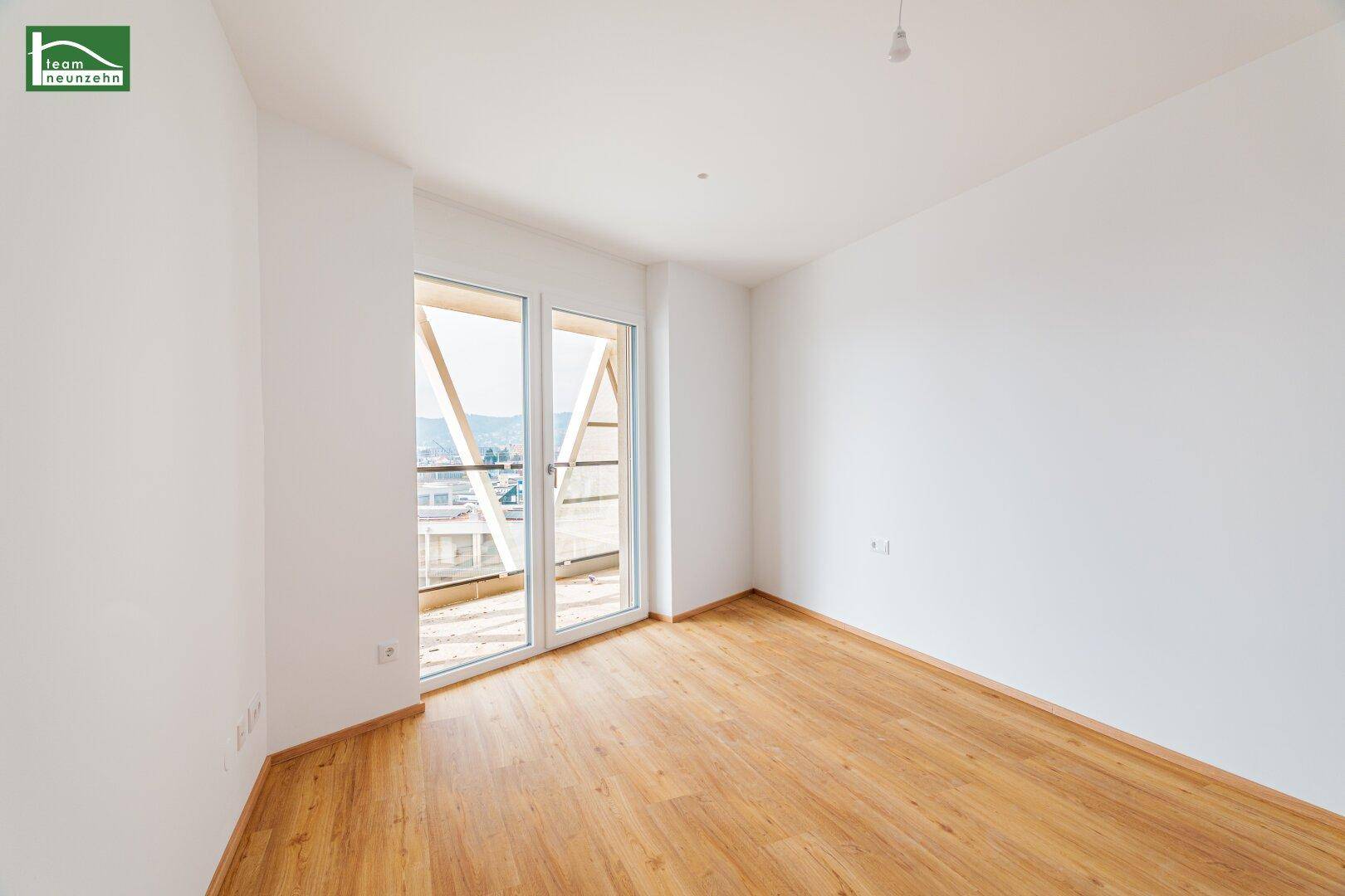 Lichtdurchfluteter Raum mit hellem Laminatboden und Zugang zum Außenbereich.