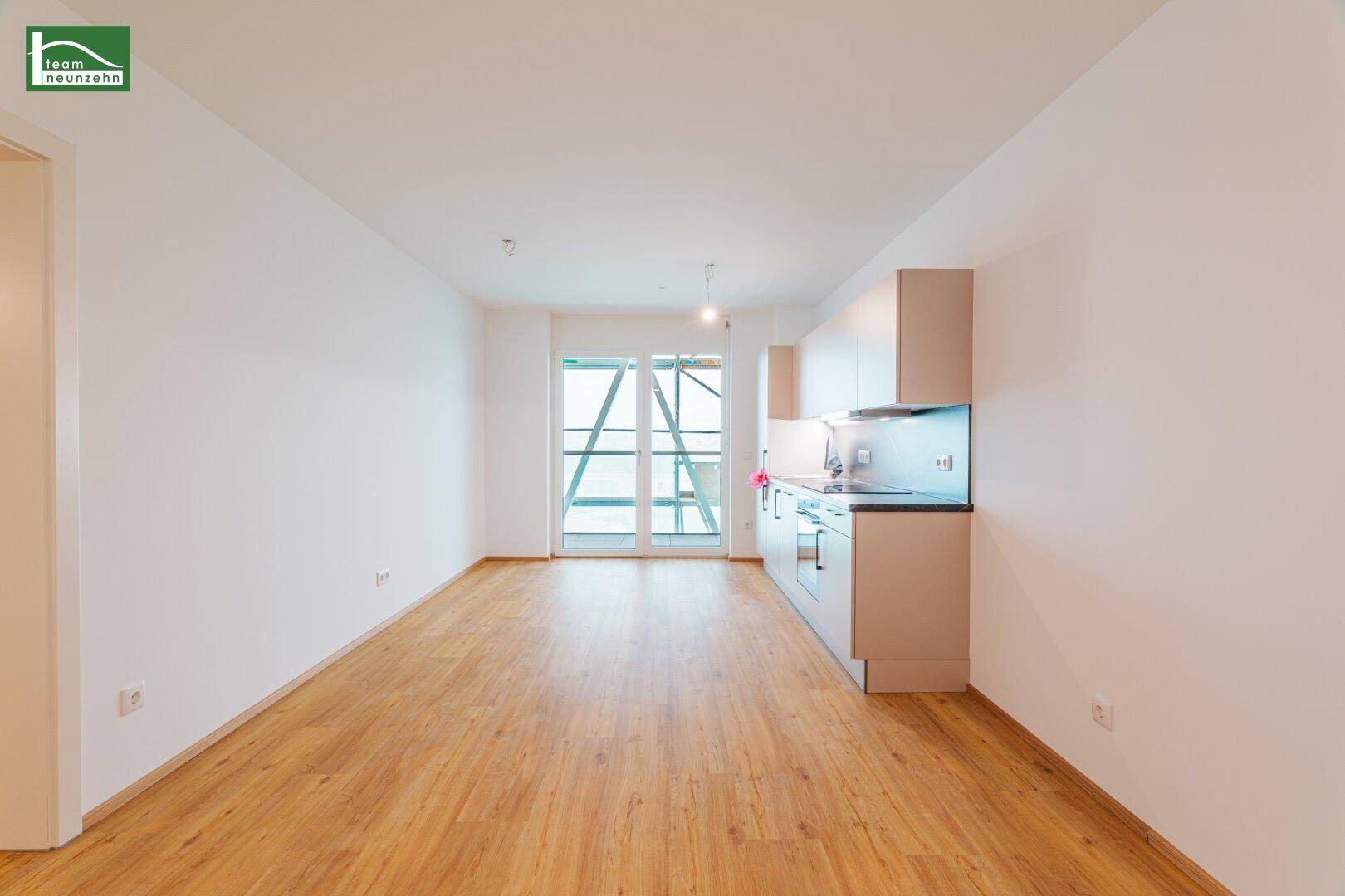 Heller Wohnbereich mit integrierter Küchenzeile, Laminatboden und Zugang zu einem Balkon.