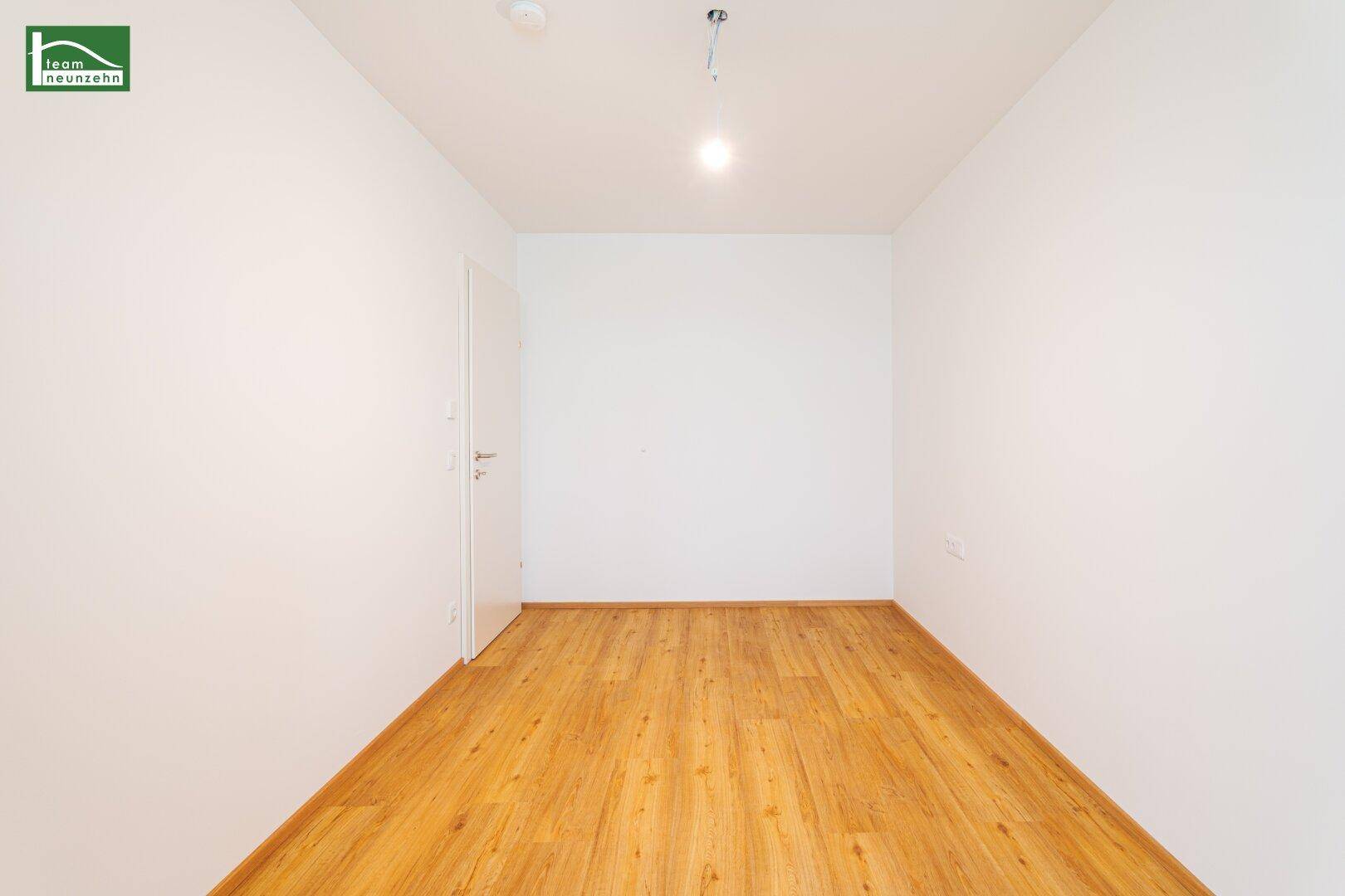 Unmöblierter Raum mit Laminatboden und weißer Tür, ideal als Kinder- oder Arbeitszimmer.