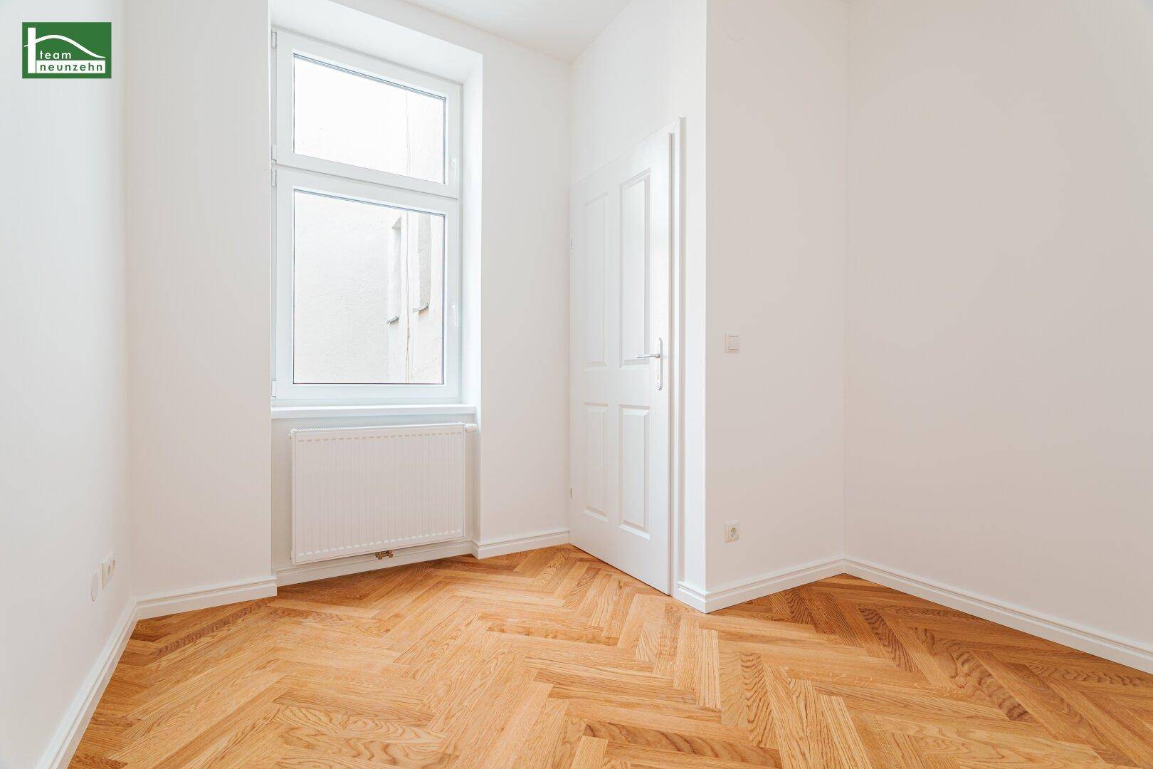 Heller Eckraum mit einem Fenster, Fischgrätparkett und weißen Wänden.