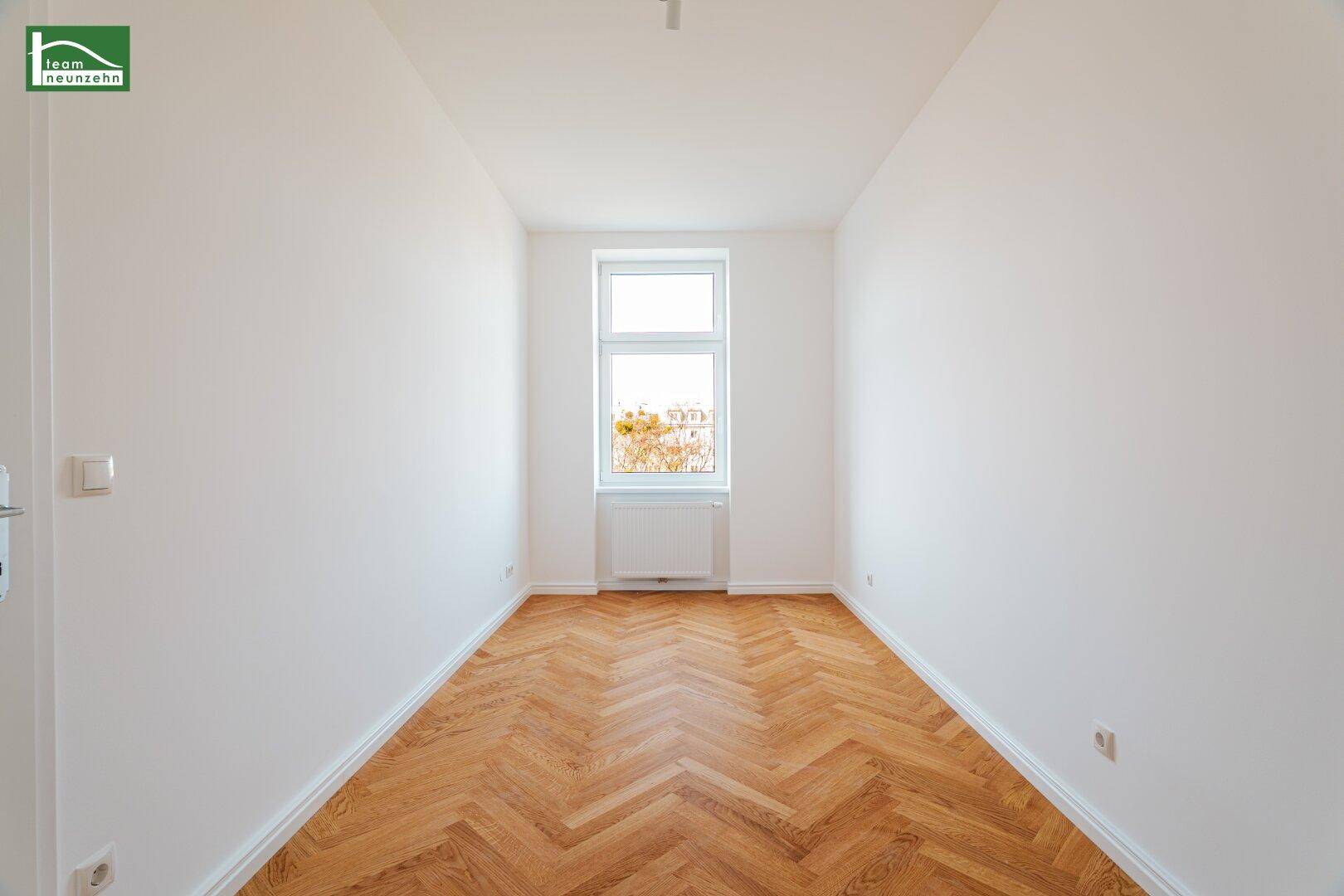 Helles, schmales Zimmer mit einem Fenster, Heizkörper und elegantem Fischgrätparkett.