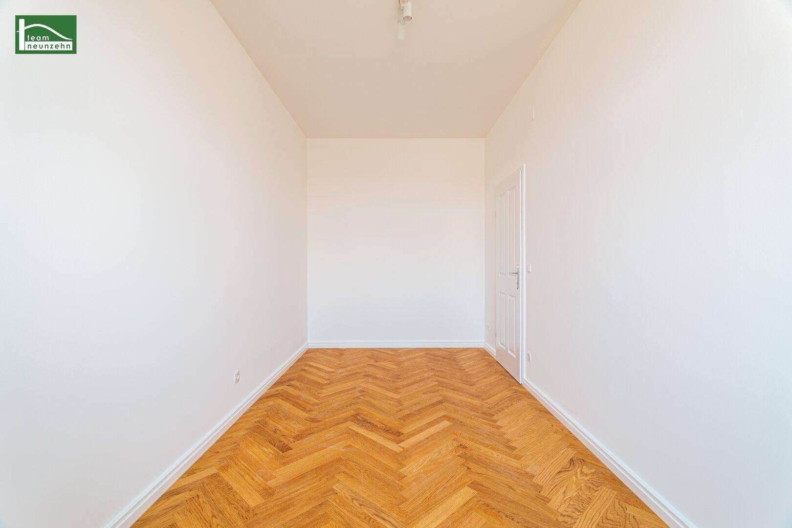 Leeres Zimmer mit Fischgrätparkett und weiß gestrichenen Wänden, ideal als Schlaf- oder Arbeitszimmer.