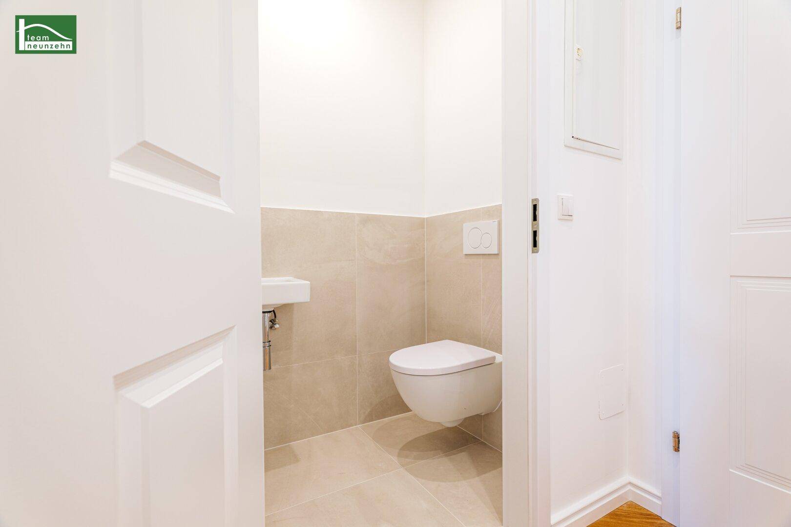 Separates Gäste-WC mit wandhängender Toilette und kleinem Waschbecken, modern gefliest.