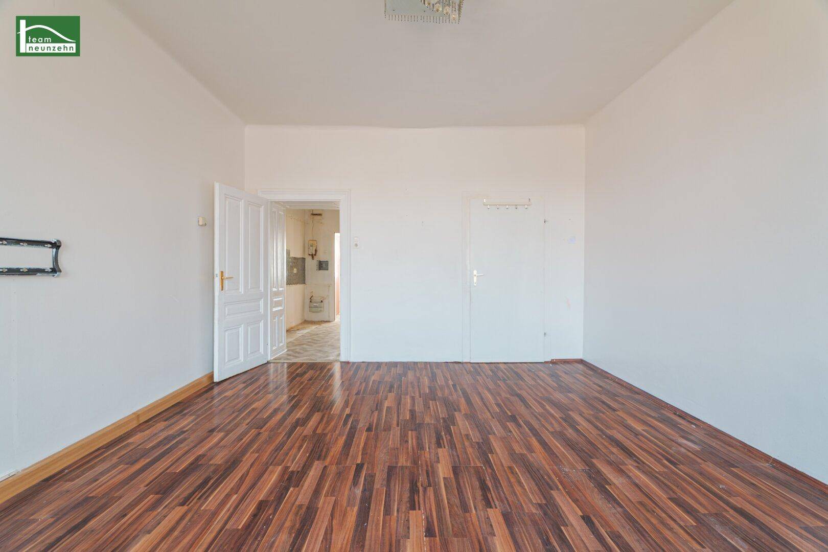 Leeres Zimmer mit dunklem Laminatboden und offener Tür zu einem weiteren Raum.
