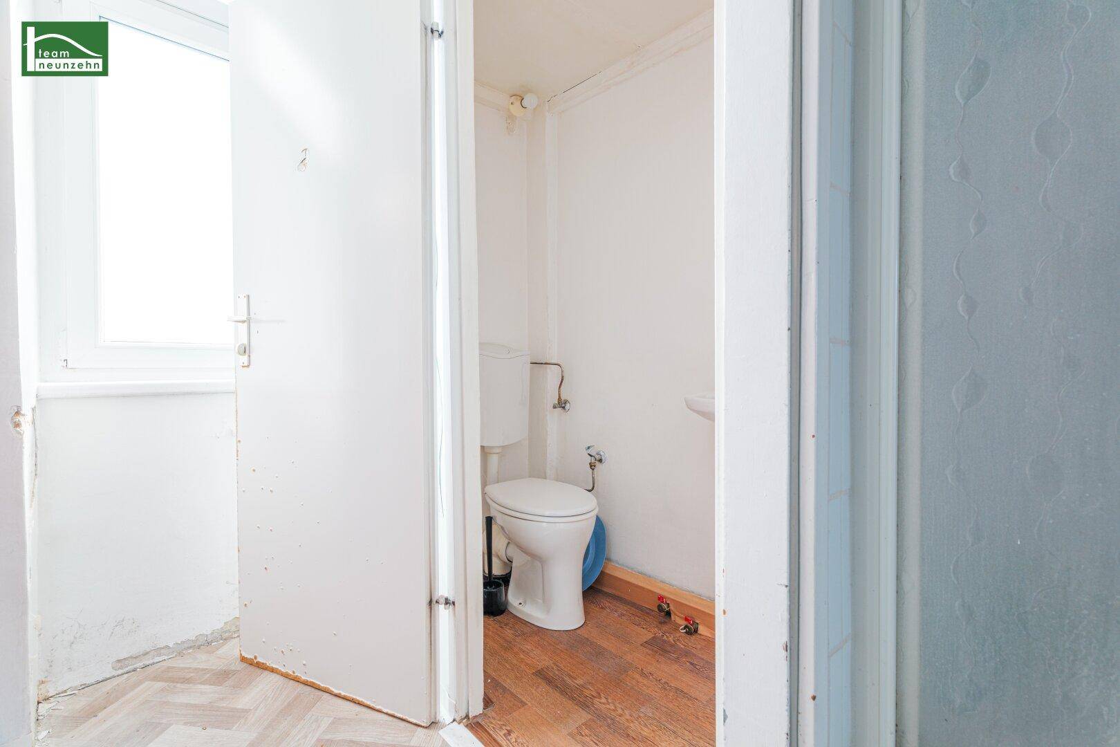 Kleines WC mit Toilette und Fenster, ausgestattet mit einfachem Laminatboden.