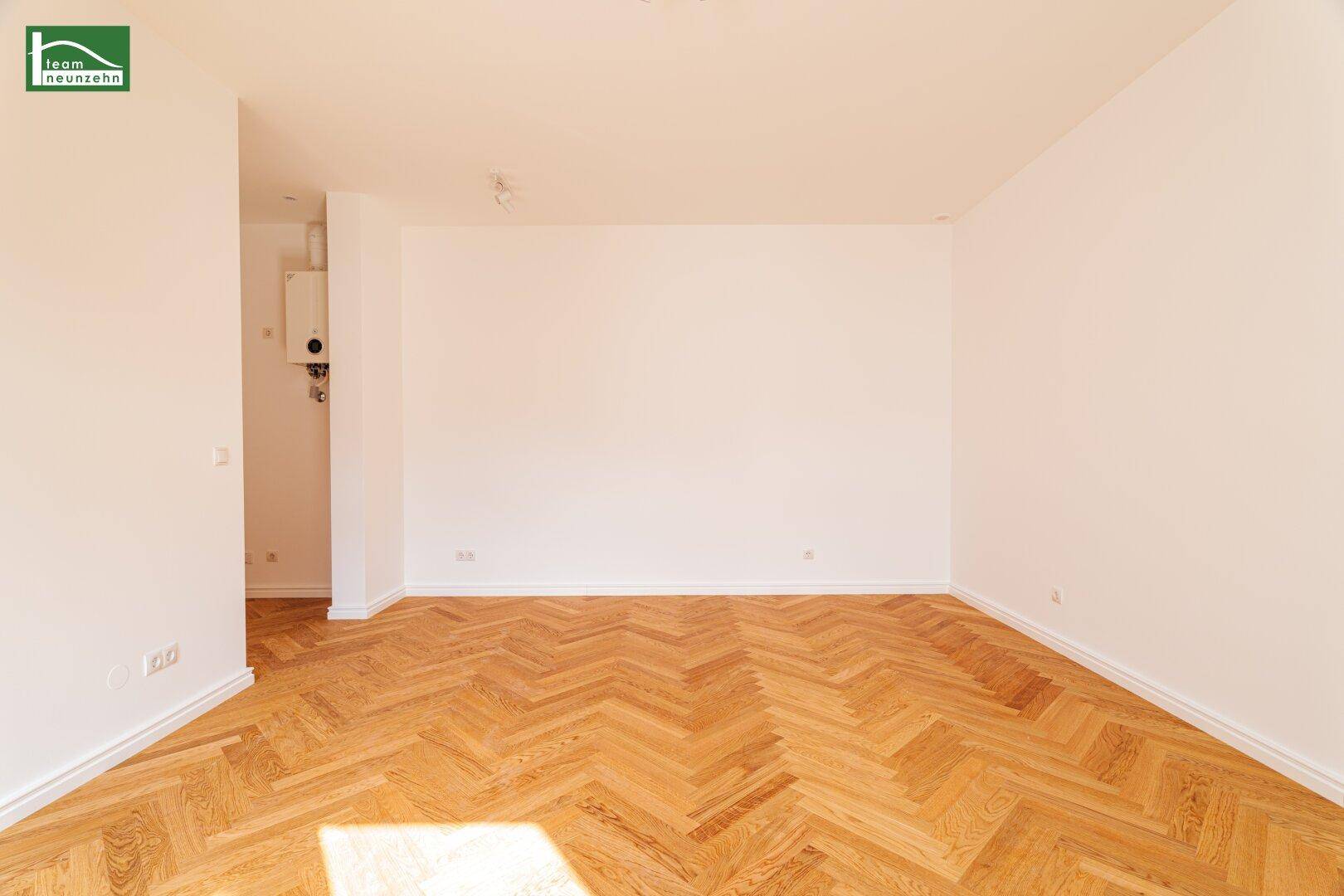 Geräumiges, leeres Zimmer mit hellem Fischgrätparkett und weiß gestrichenen Wänden, bereit zur Einrichtung.