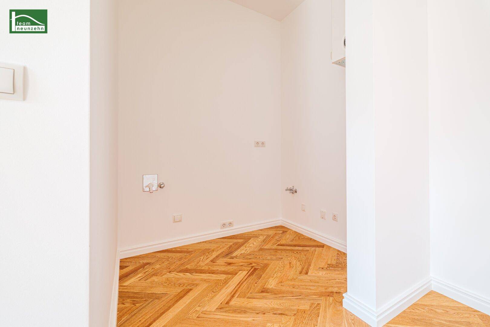 Ecke eines leeren Raumes mit Fischgrätparkett und Anschlüssen, die verschiedene Nutzungsmöglichkeiten bieten.