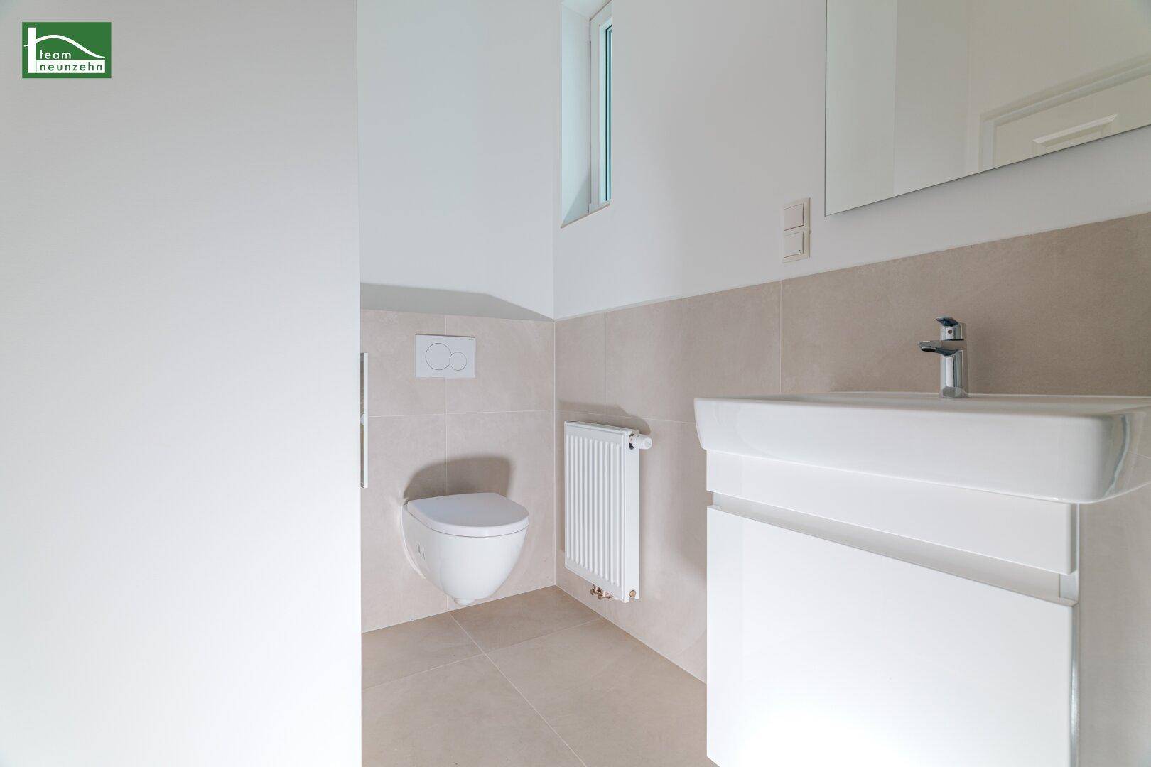 Helles Badezimmer mit wandhängendem WC, Waschbecken und Fenster, ausgestattet mit modernen Fliesen.