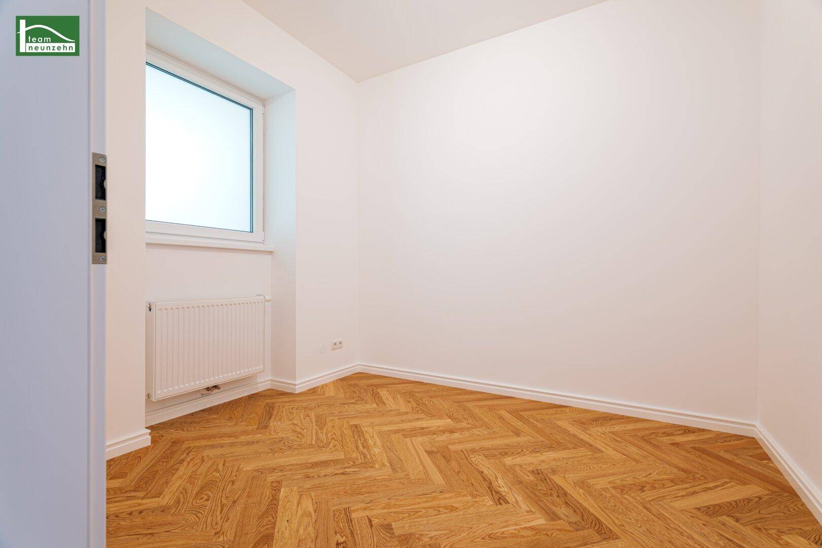 Kleinerer Raum mit einem Fenster, Fischgrätparkett und weiß gestrichenen Wänden.