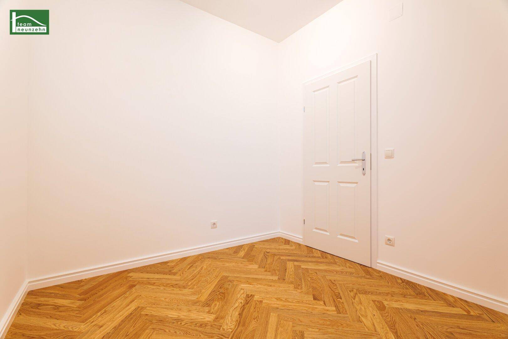Leeres Zimmer mit Fischgrätparkett, weißer Tür und sauber gestrichenen Wänden.