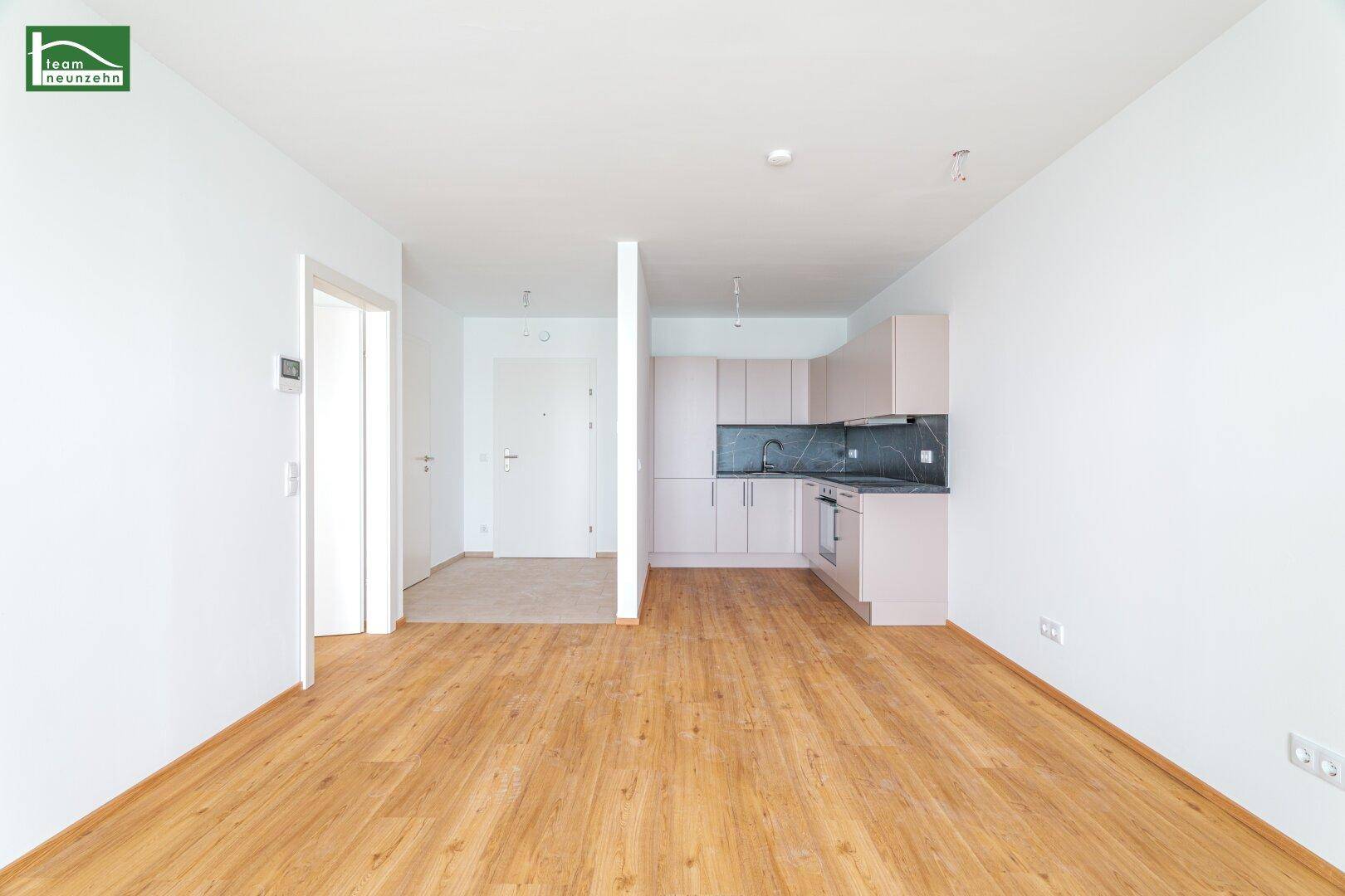 Heller offener Wohnbereich mit Holzboden und integrierter Küchenzeile in modernem Design.