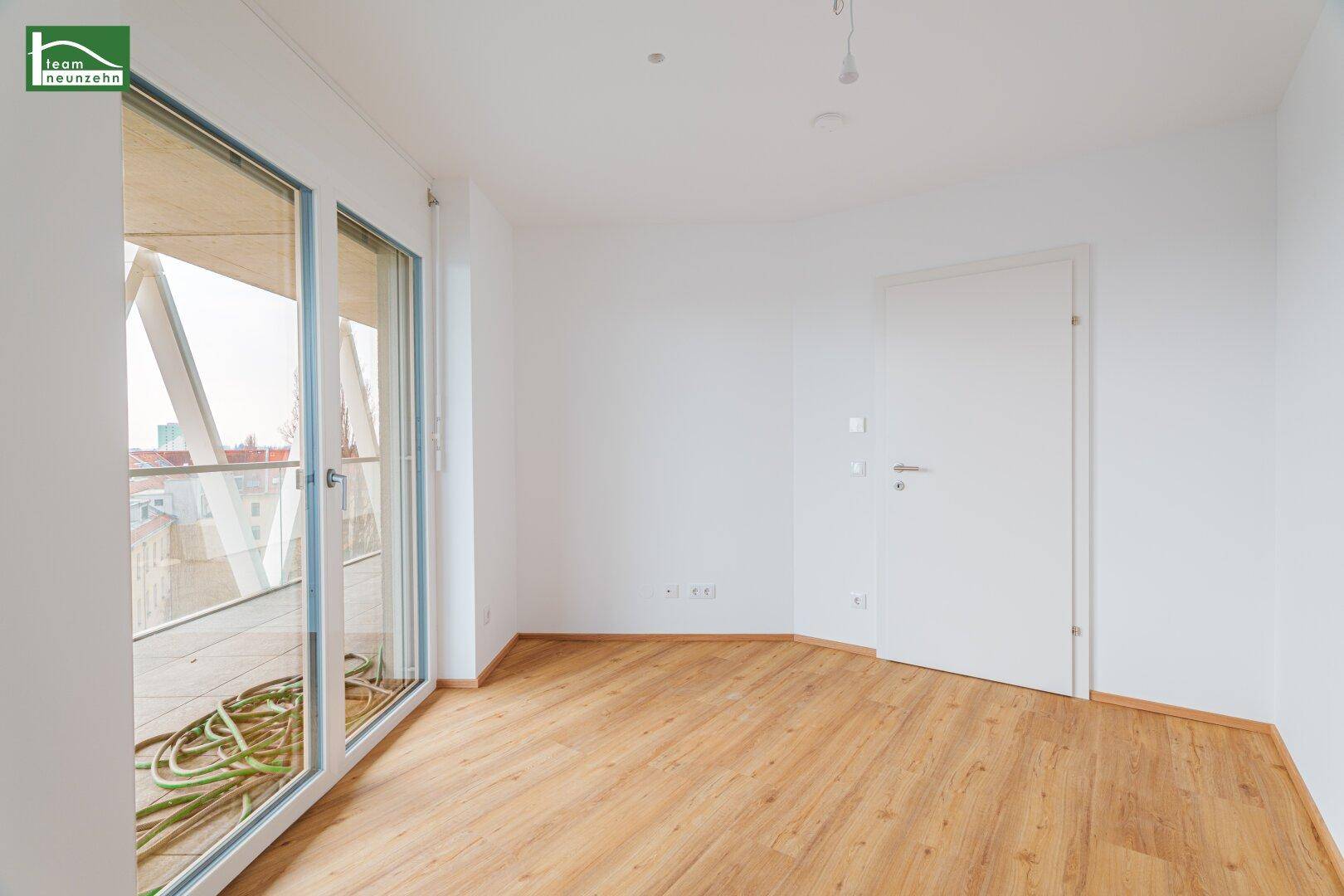 Heller Raum mit Parkettboden und Fenstertüren, die zu einem Außenbereich führen.