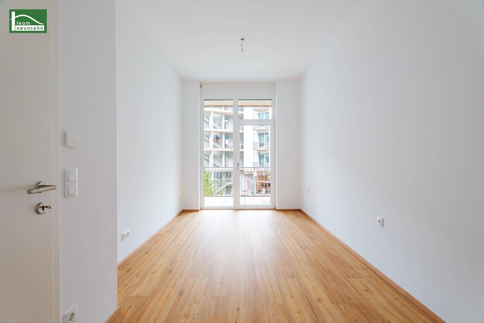 Leeres Schlafzimmer mit Holzboden und großem Fenster, das Zugang zu einem Balkon bietet.