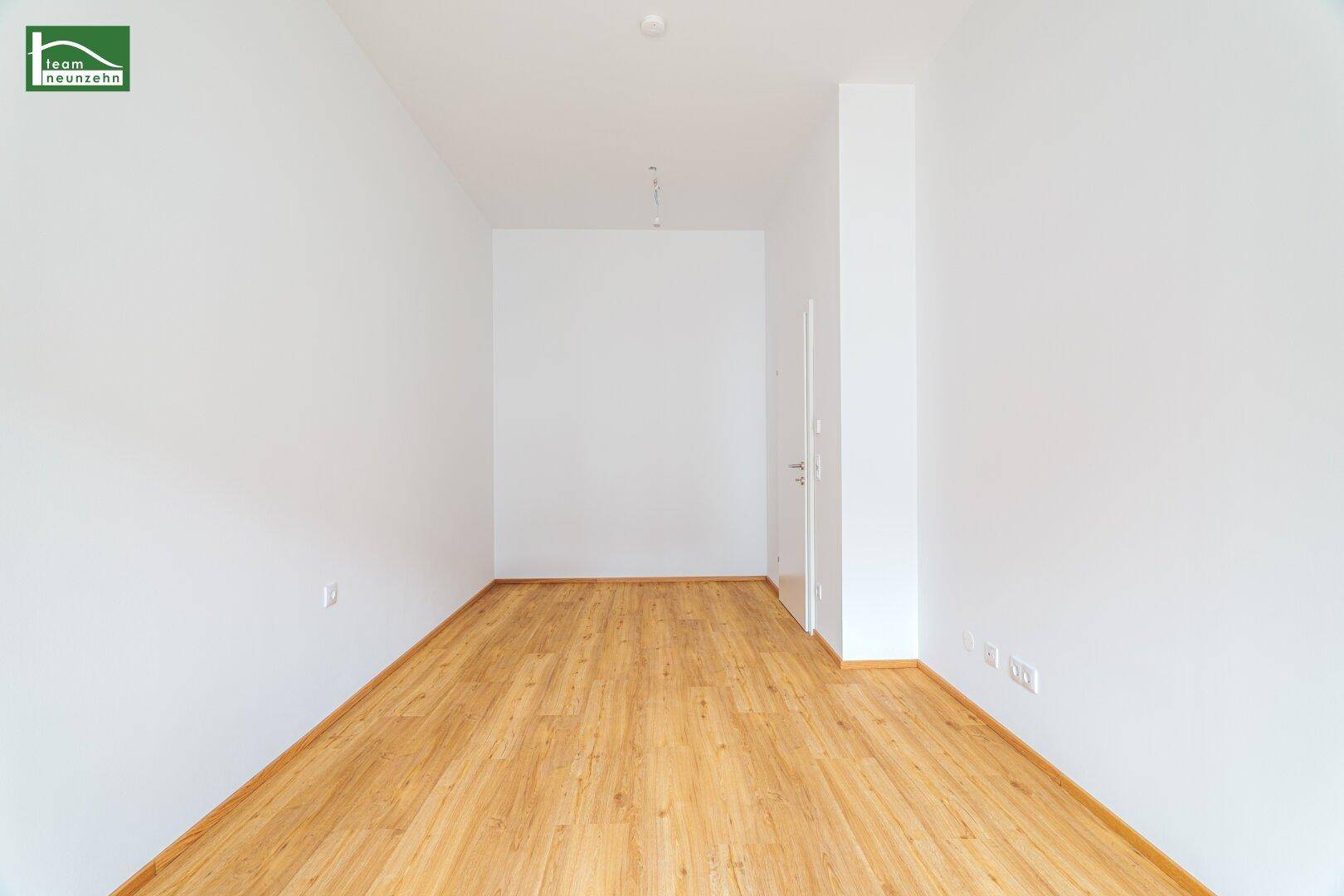 Heller, leerer Flur mit Holzboden und weiß gestrichenen Wänden.