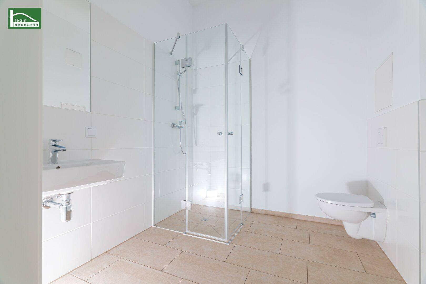 Modernes Badezimmer mit Duschkabine, Waschbecken und wandhängendem WC, hell gefliest.